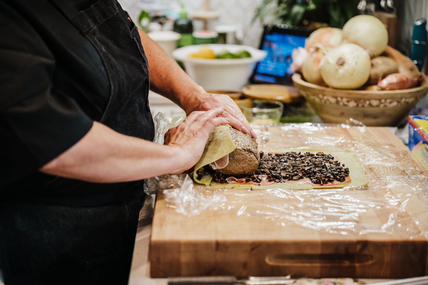 Hands kneading and shaping dough on a wooden cutting board dusted with flour.