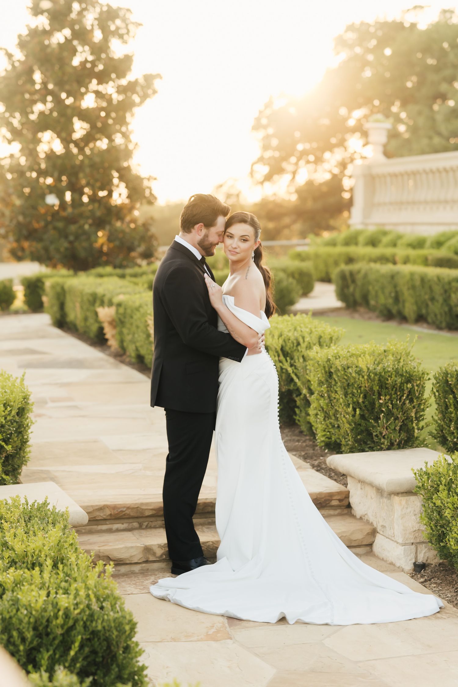 Golden hour wedding portraits along manicured garden path with flowing bridal gown.