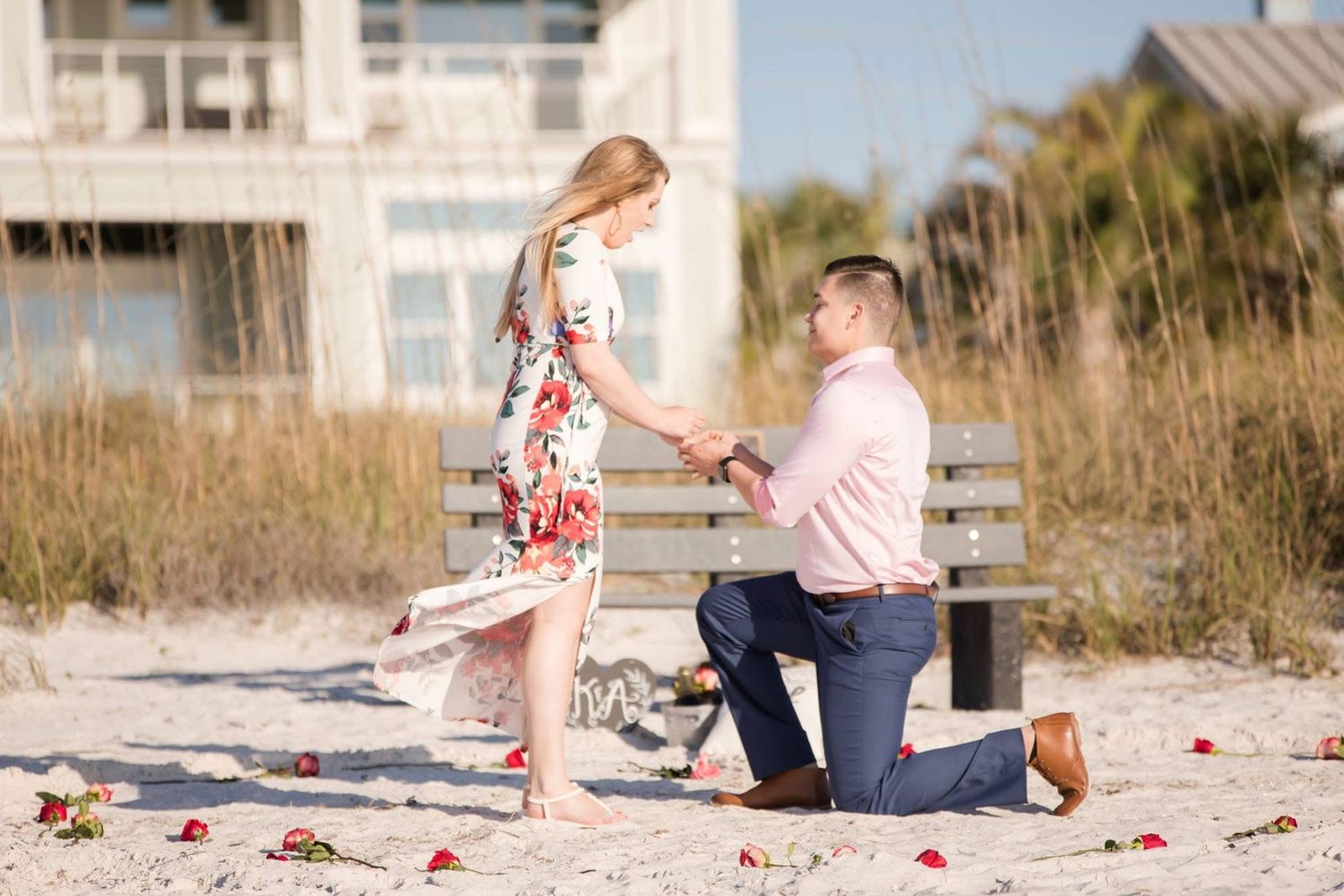 Romantic beach engagement session with rose petals scattered on sandy shore.