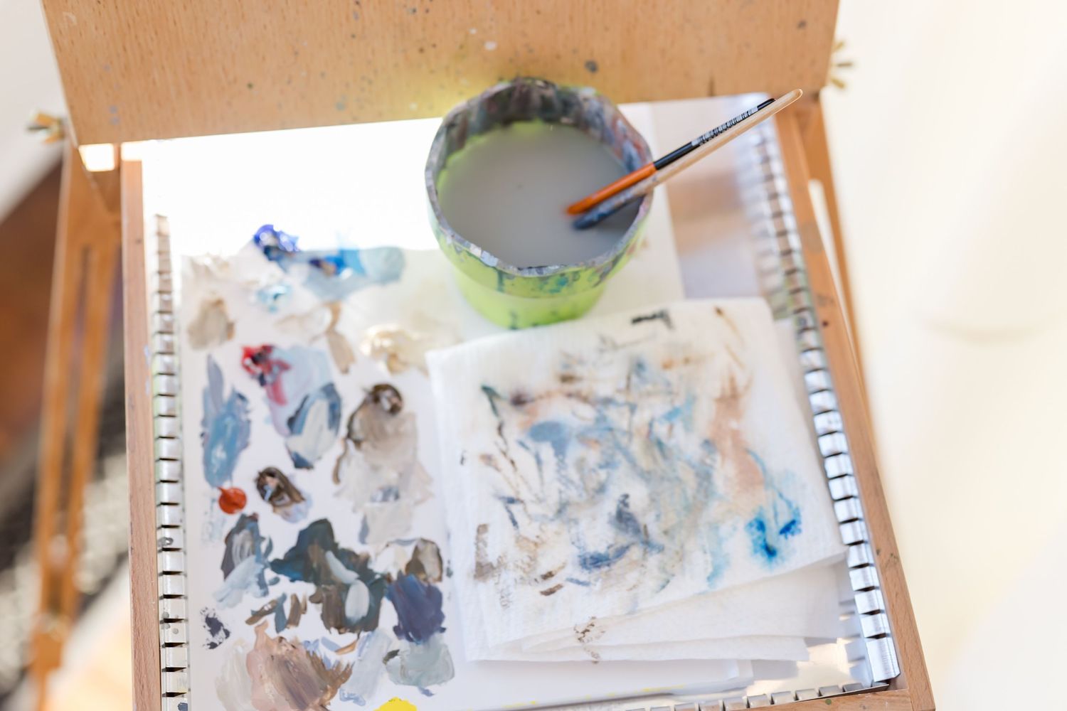 Artist's palette and tools laid out on a wooden surface showing watercolor paint mixtures.