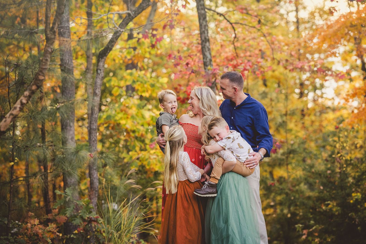A fall family photo session features people in coordinated outfits among colorful autumn trees.