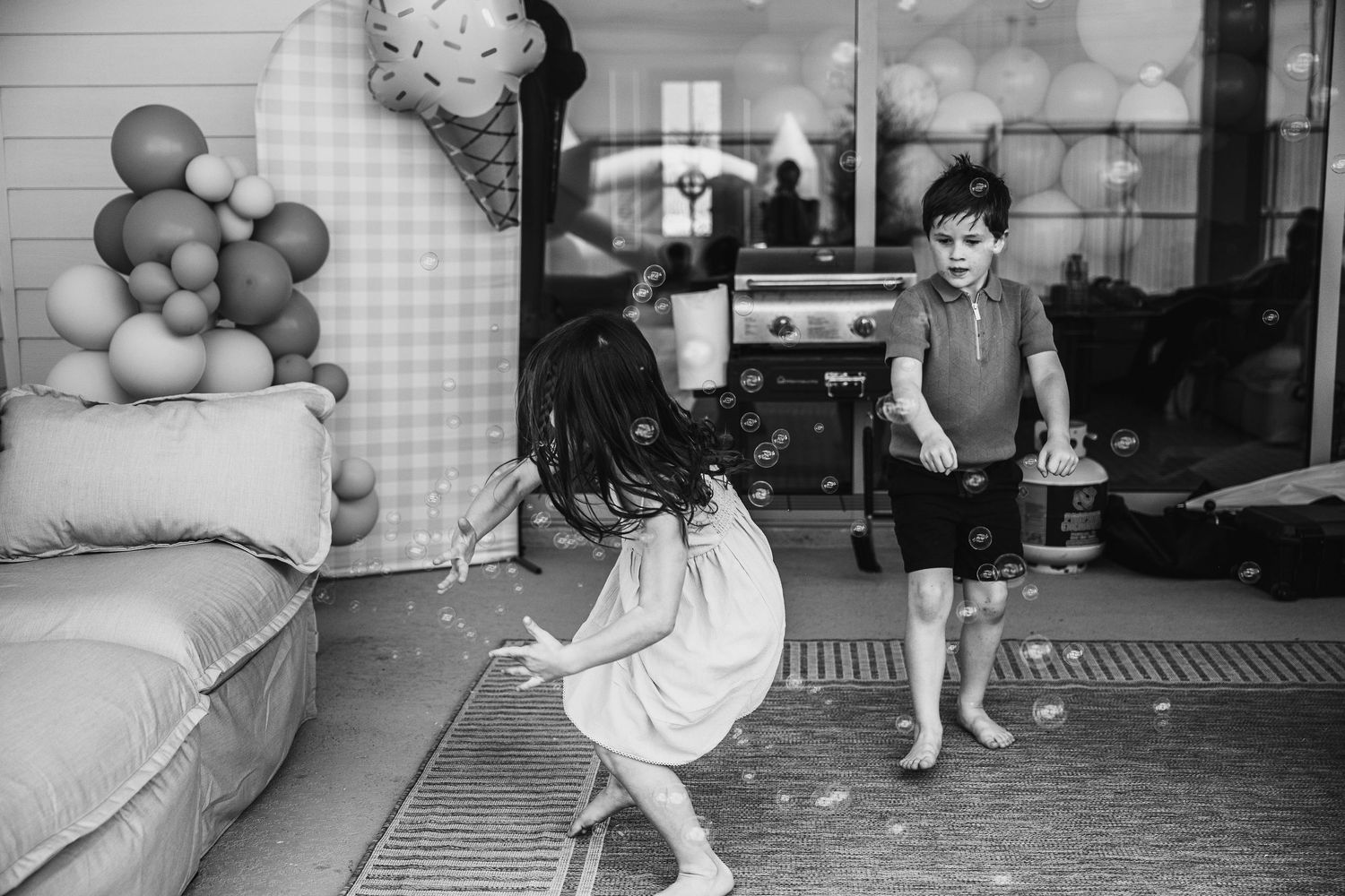 Two children playing outdoors near balloon decorations in a black and white candid photo.