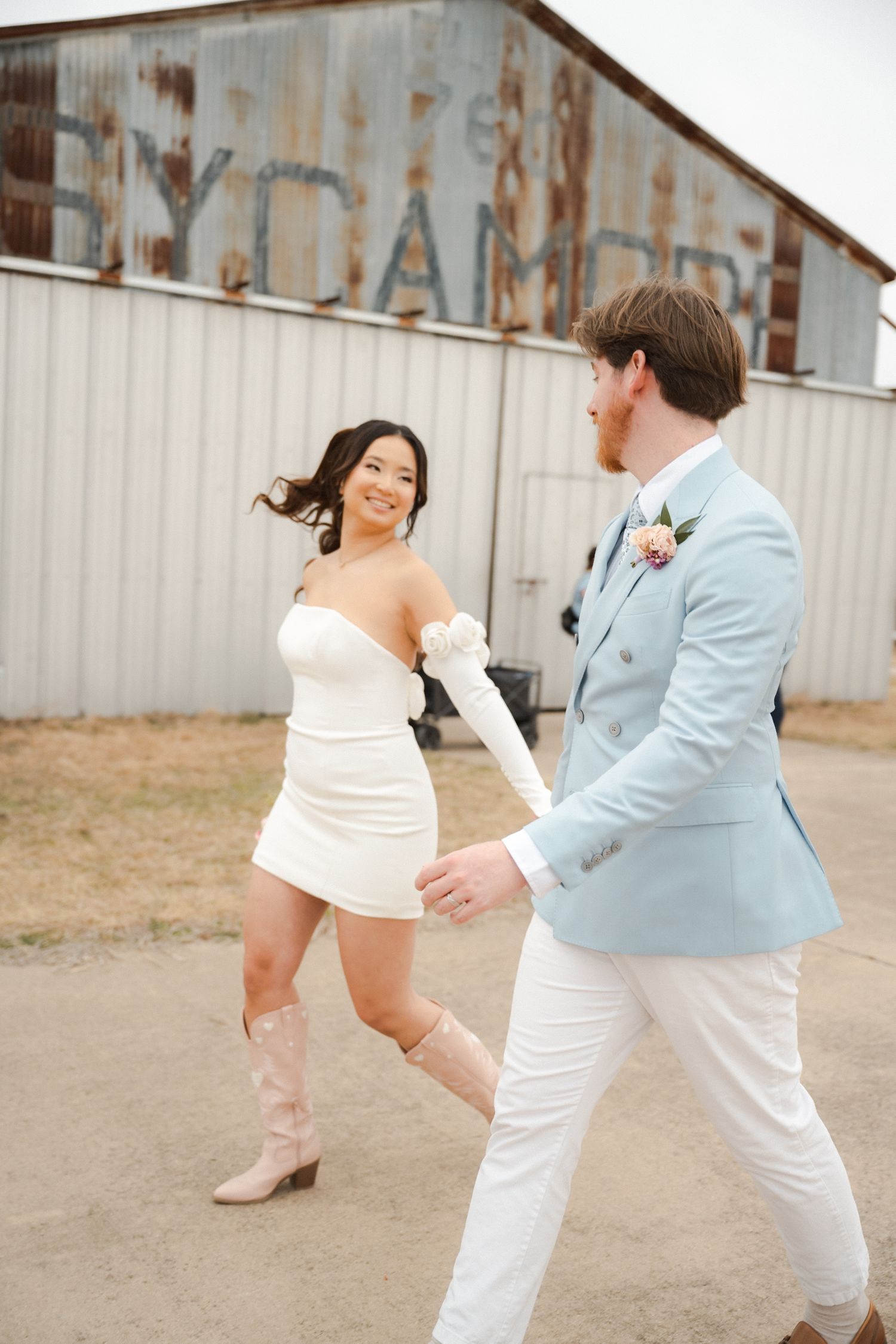 A couple in light-colored outfits dance playfully in front of a rustic metal wall in a series of candid shots.