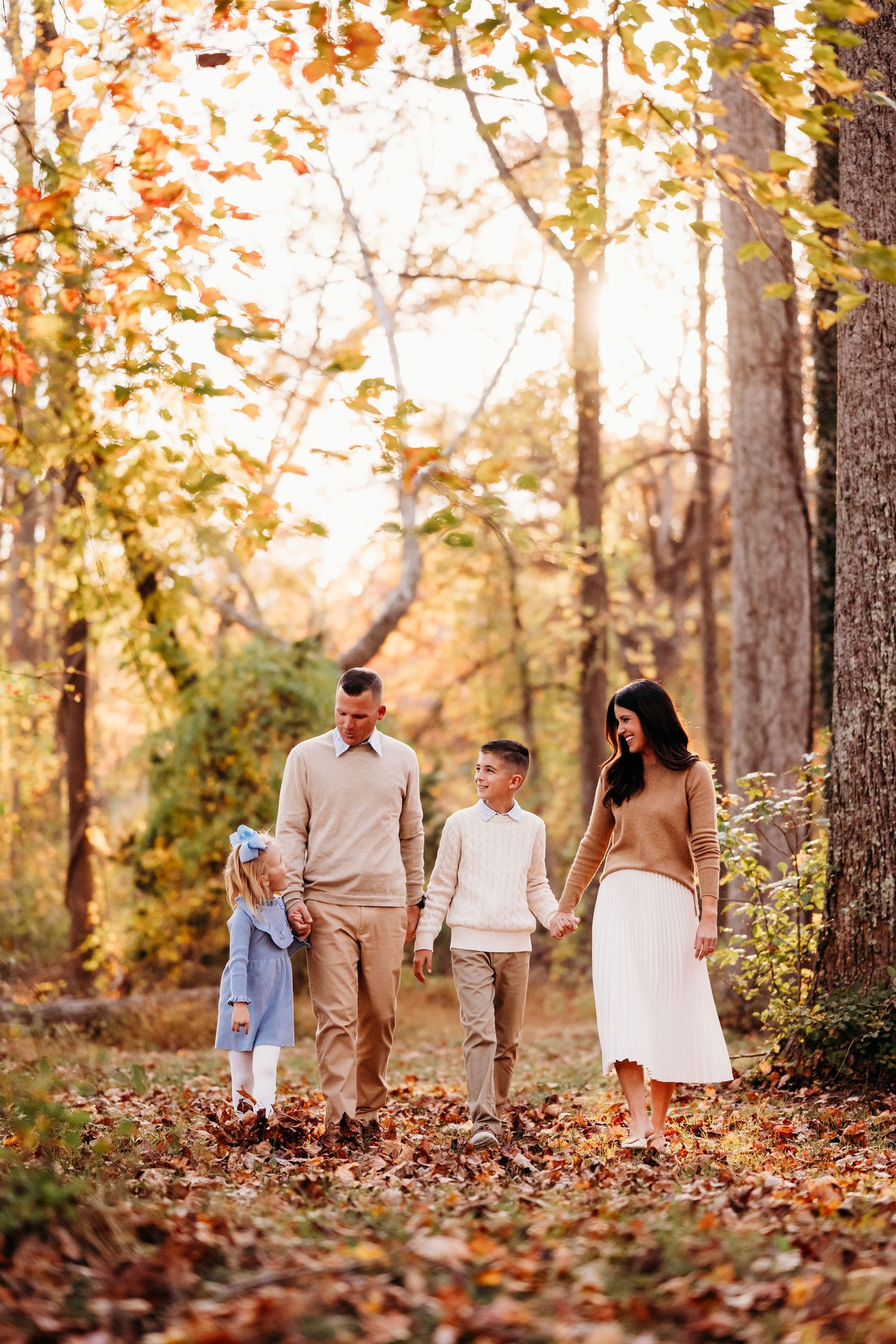 A group walks through fallen leaves on a wooded path during golden hour.