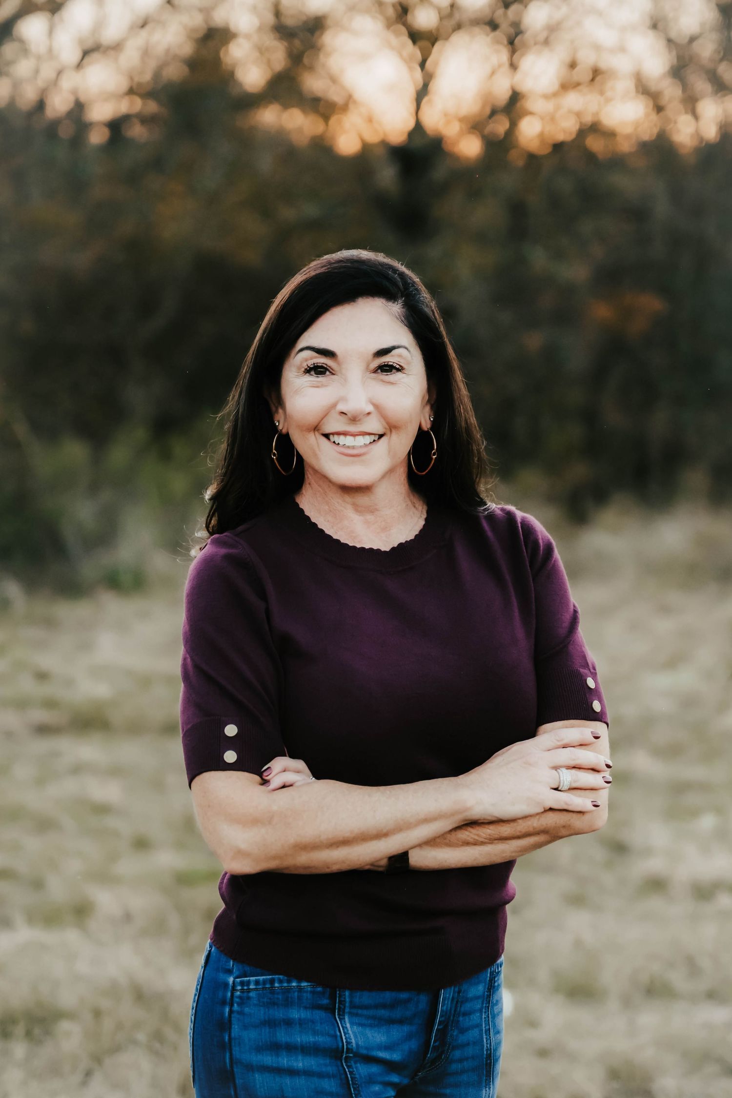 Person in a purple sweater and jeans poses outdoors at sunset in a natural field setting.
