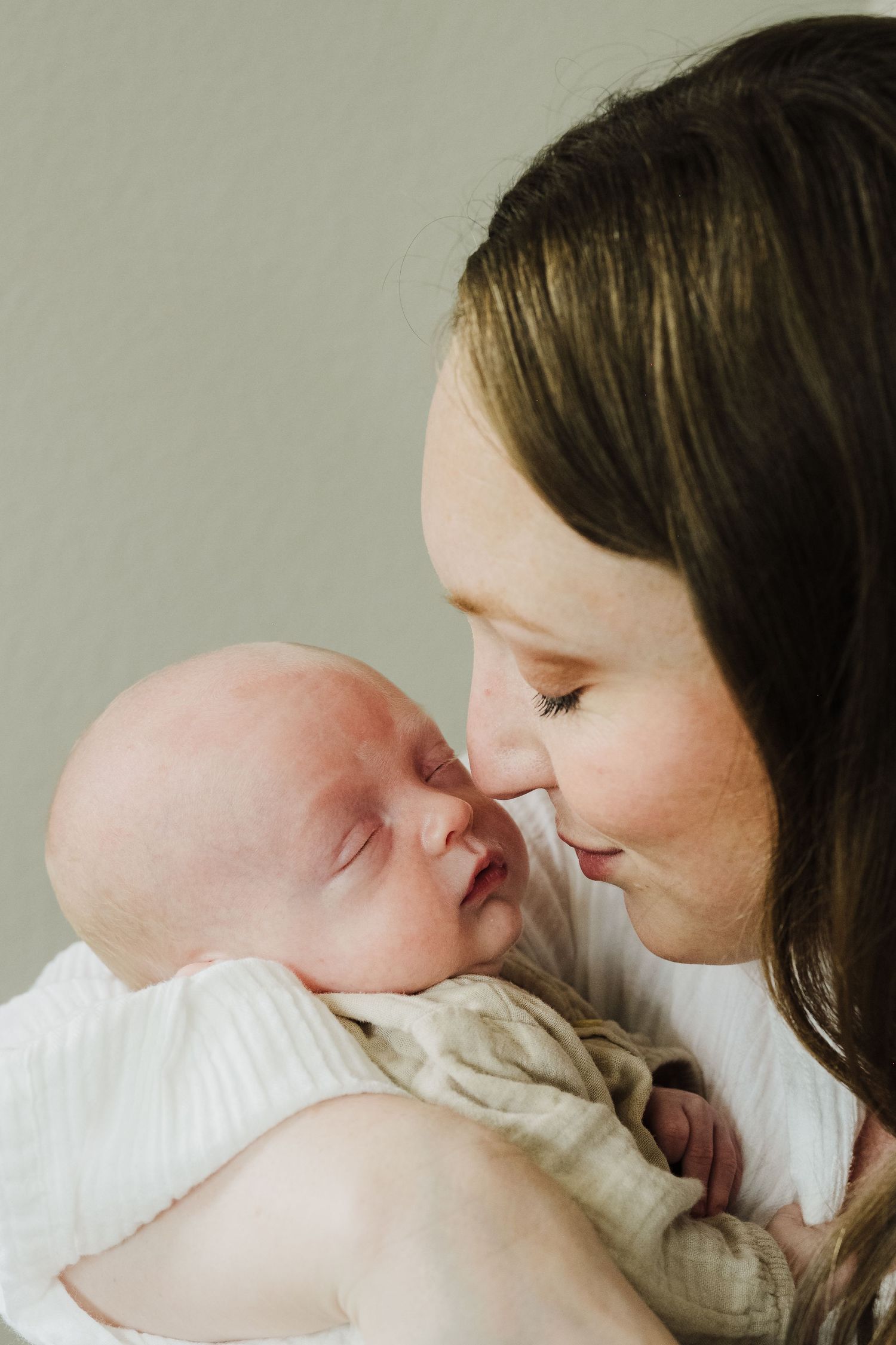 A tender moment between parent and newborn baby in soft natural light against neutral background.