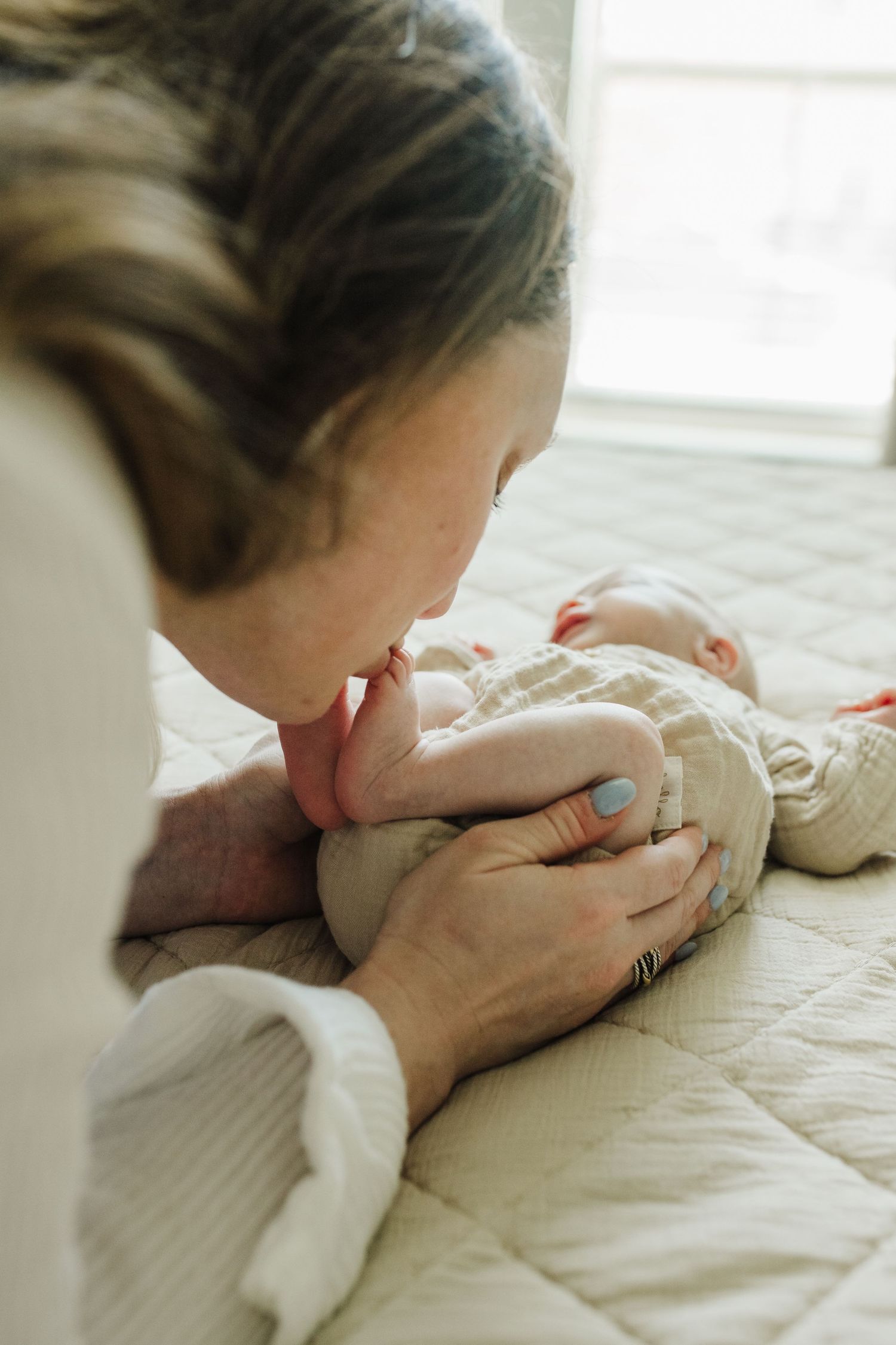 A series of photos showing a person gently kissing a white baby's foot on a textured beige bedspread.