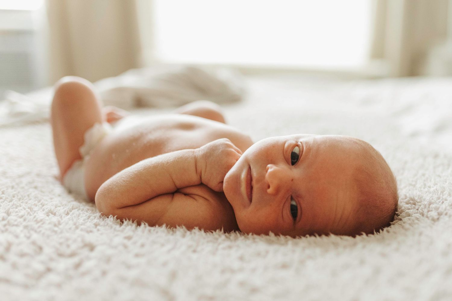 Sweet newborn baby lying on soft white blanket in natural light.