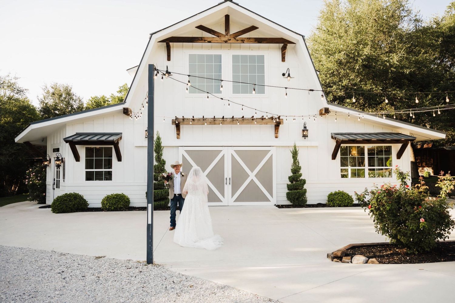 Modern white barn-style garage with cross-pattern doors and architectural s a charming farmhouse exterior. Trickle Creek, by Knot & Wing