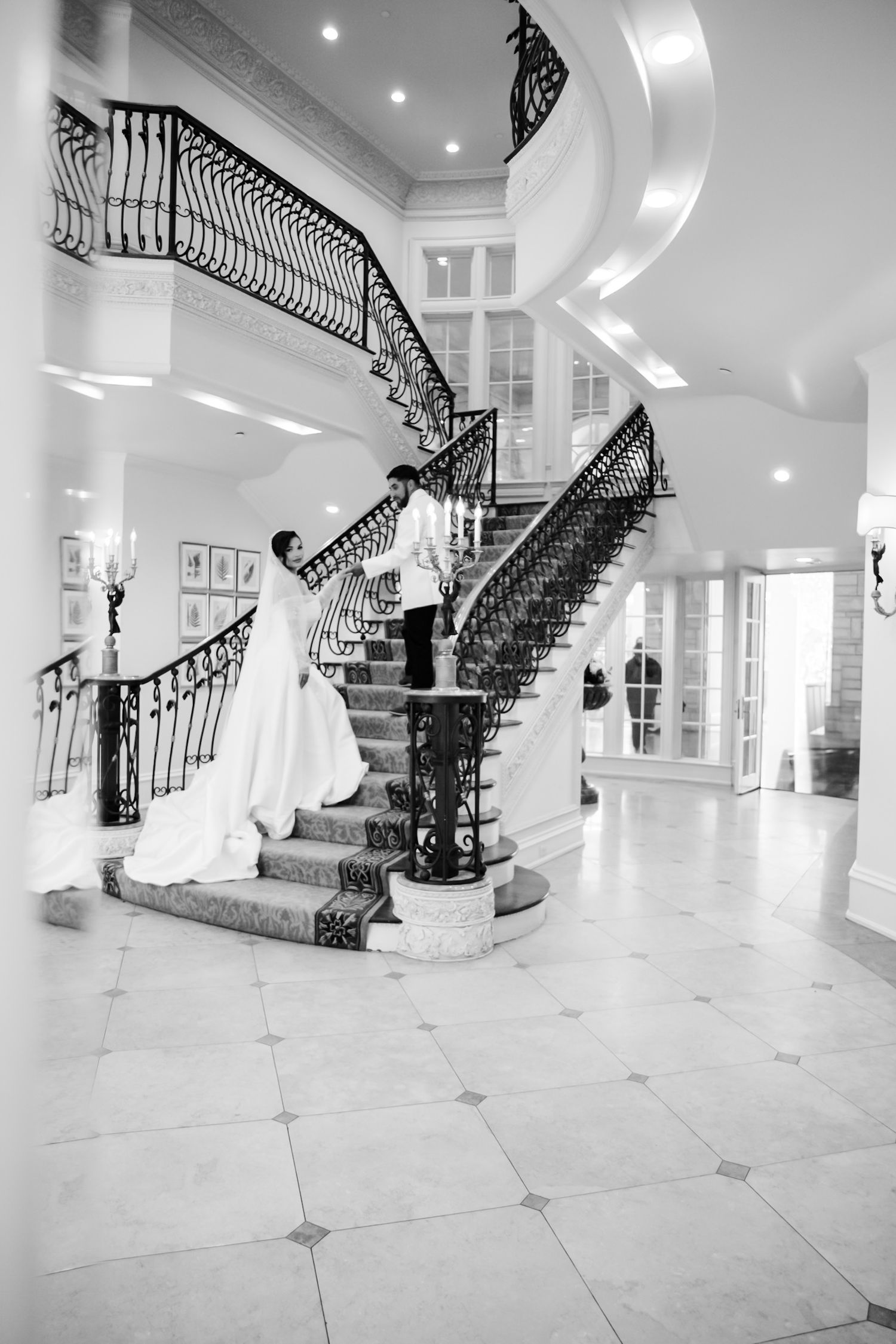 Grand white marble staircase with ornate black iron railings in an elegant foyer.