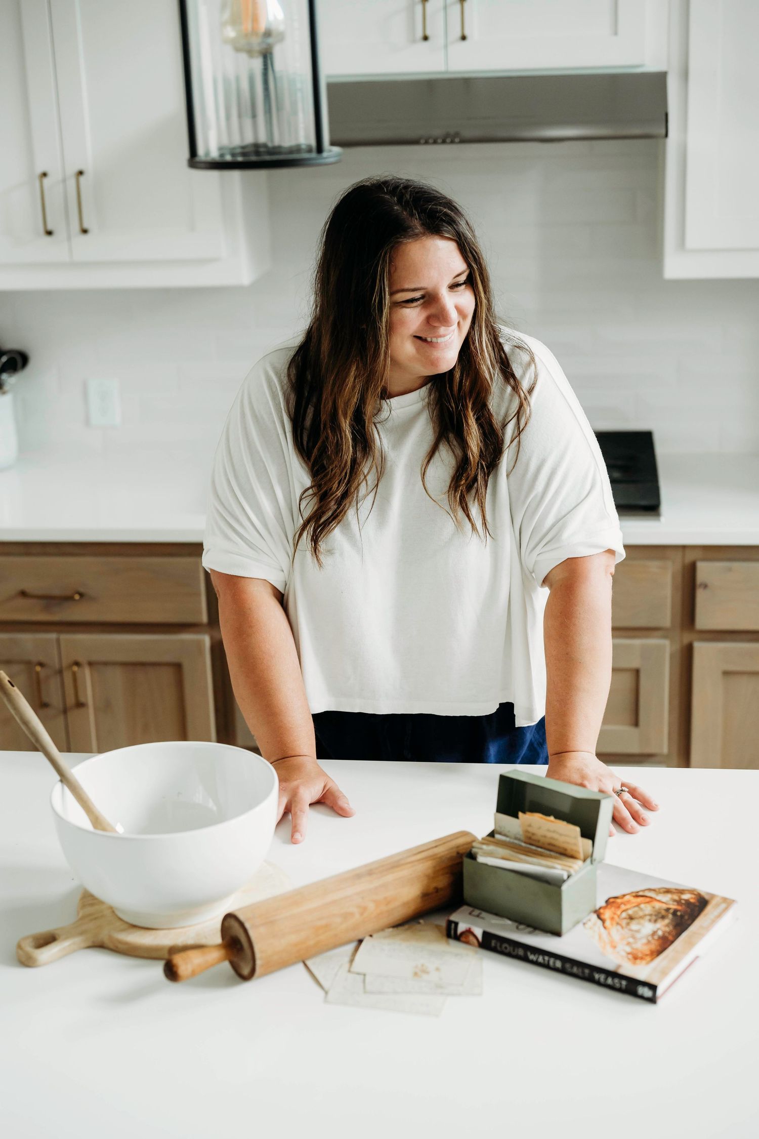 Person in white shirt preparing food in modern kitchen with white cabinets.