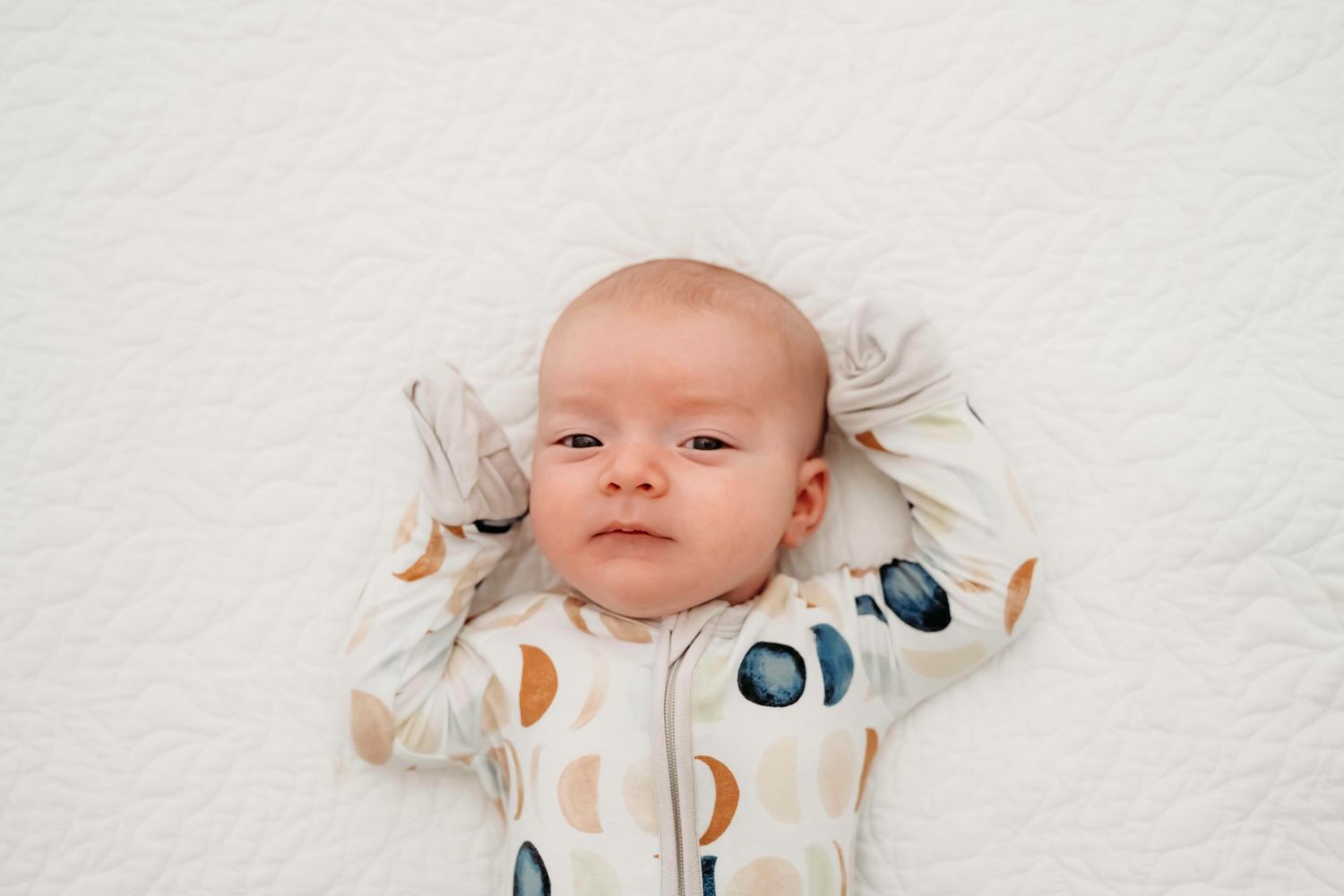 Baby lying on white fabric wearing onesie with graphic print.