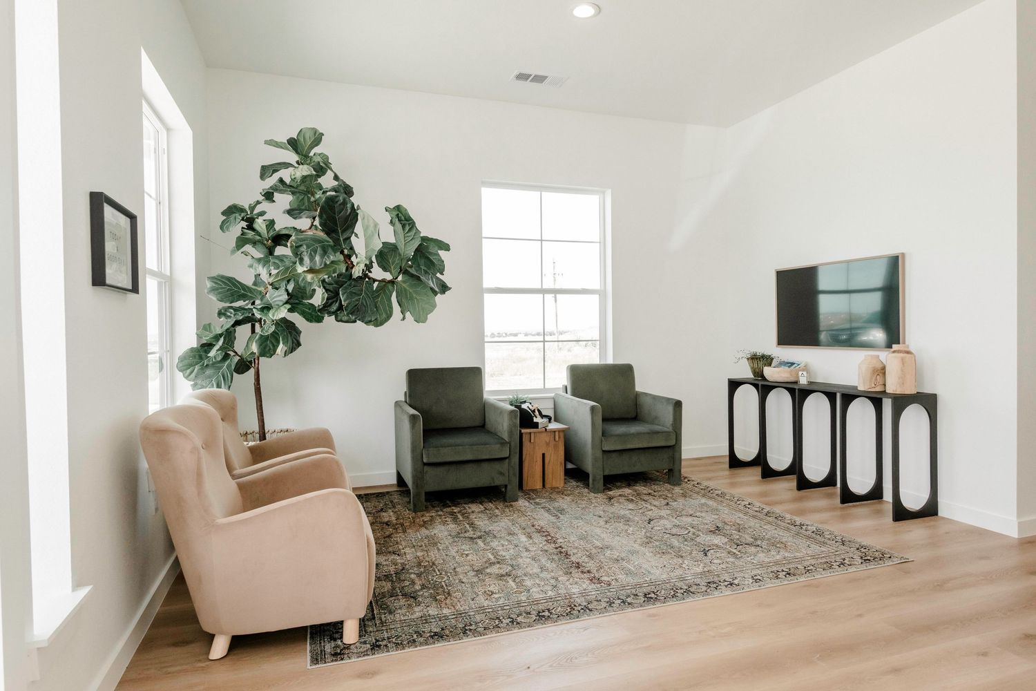 Modern living room interior with white walls, beige armchair, and potted fiddle leaf fig plant in corner.
