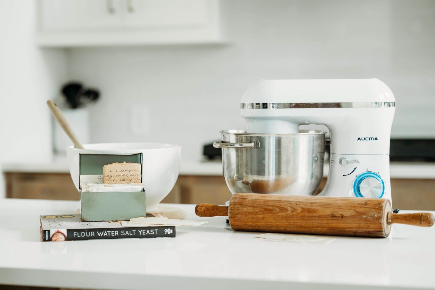 Minimalist white kitchen counter with wooden cutting board and glass jar displaying clean modern design aesthetic.
