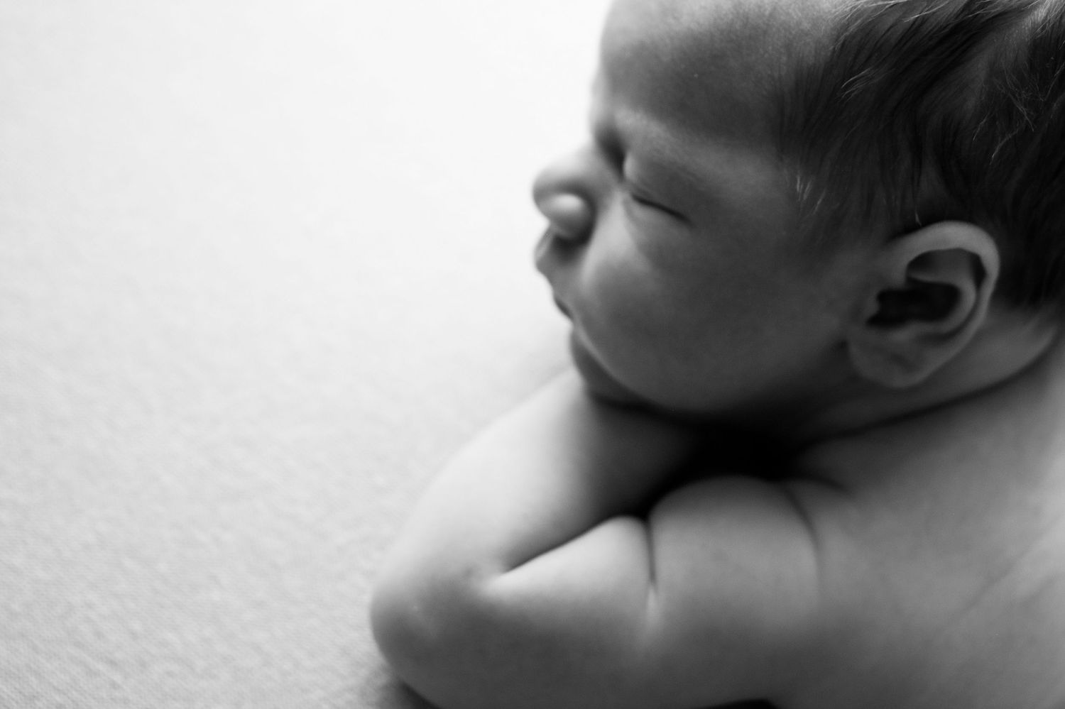 Black and white newborn baby sleeping peacefully, curled up with arms tucked under chin in serene portrait.