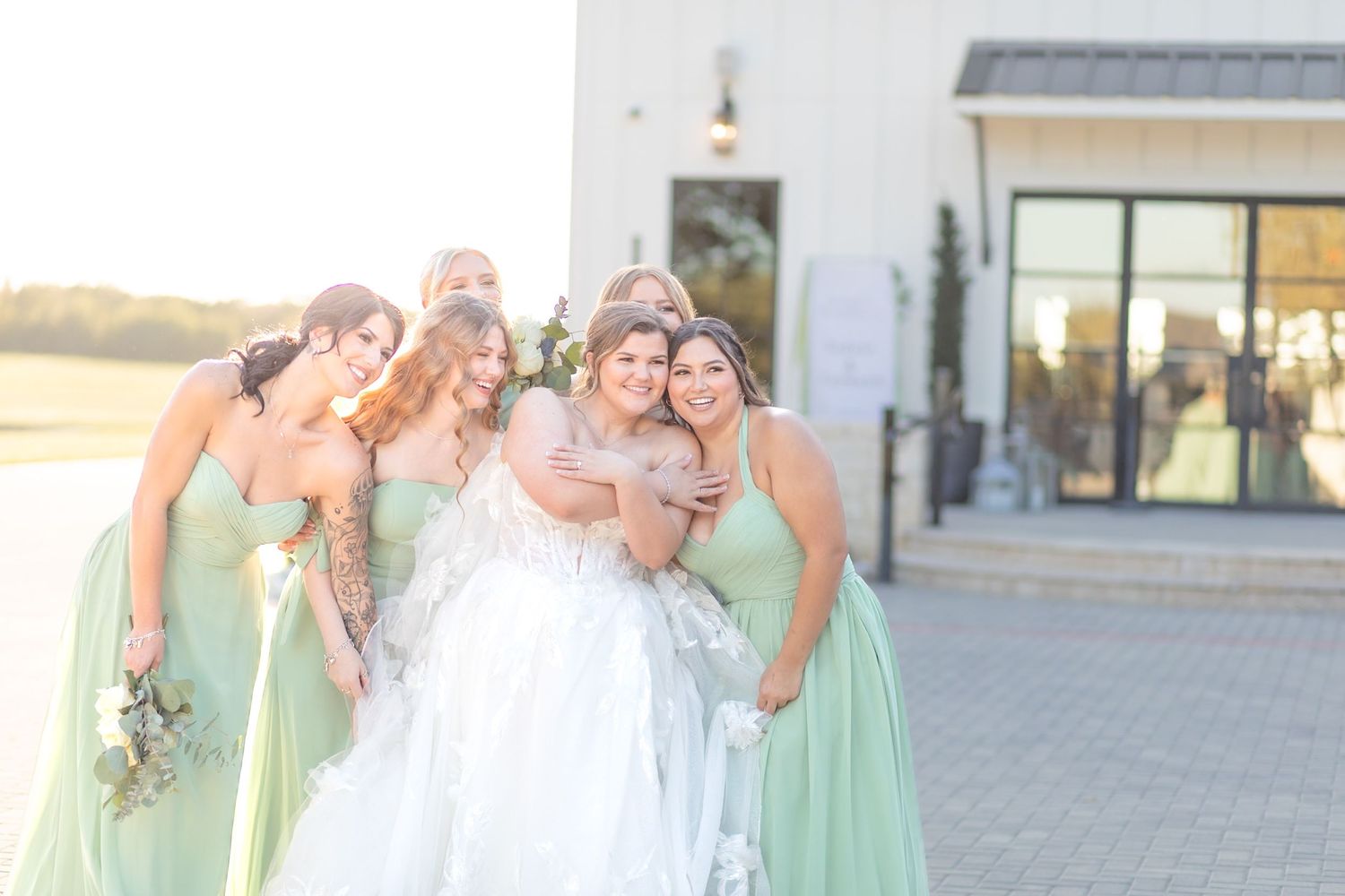 Wedding party in mint green bridesmaid dresses poses together outdoors on a sunny day.
