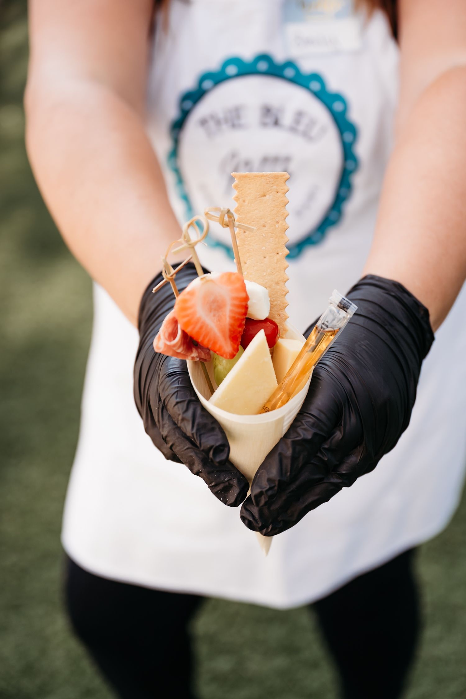 A series of hands wearing black gloves holding and scooping ice cream into waffle cones against a blurred green background.