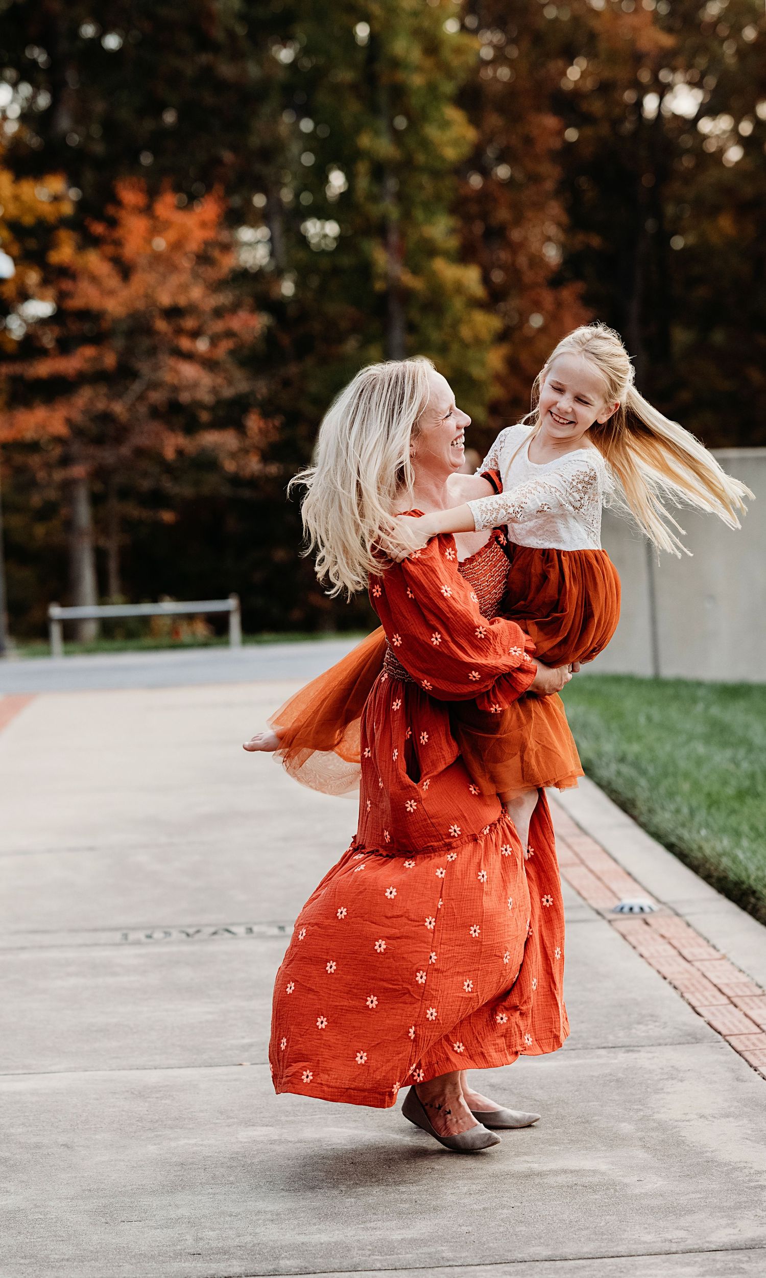 A playful dance captured in a spinning motion on a concrete path with fall foliage in the background.
