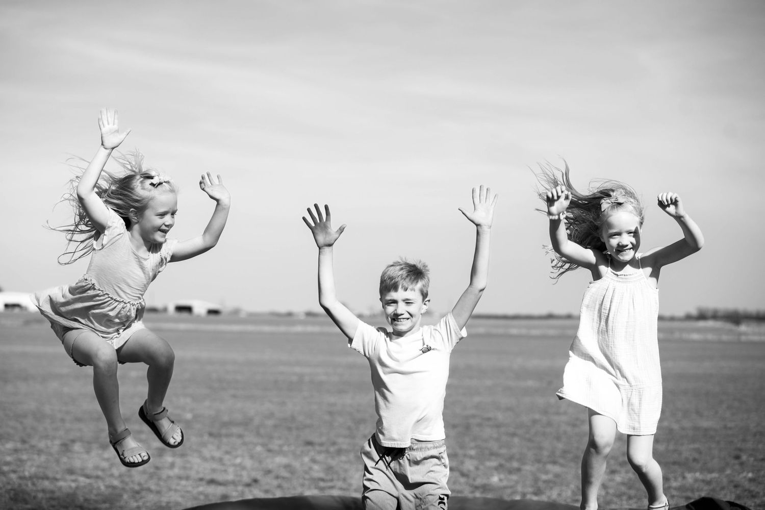 Three children laughing and jumping together outdoors during a family photography session in Southwest Missouri.