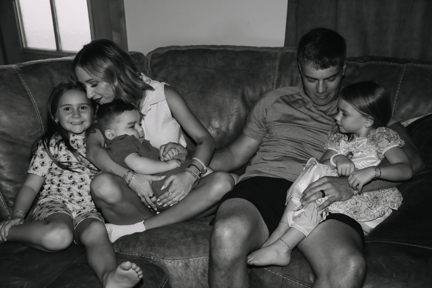 Black and white family photo of parents with three young children relaxing together on a couch.