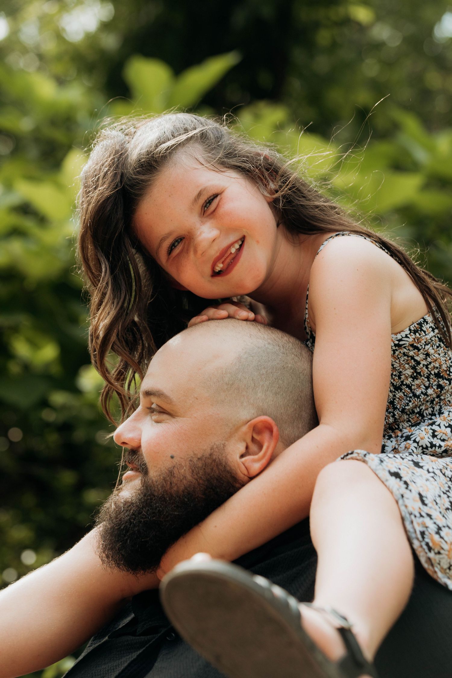 young girl smiling while sitting on her fathers shoulders during a playful outdoor photo session in Joplin, Missouri.