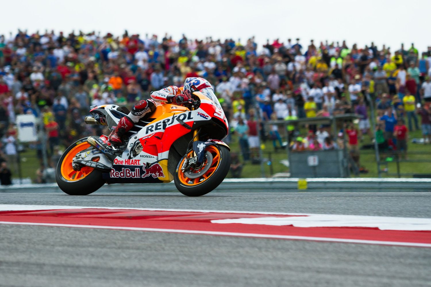 MotoGP motorcycle racer, Marc Marquez, leans into a sharp turn during a high-speed race with spectators watching from the sidelines.