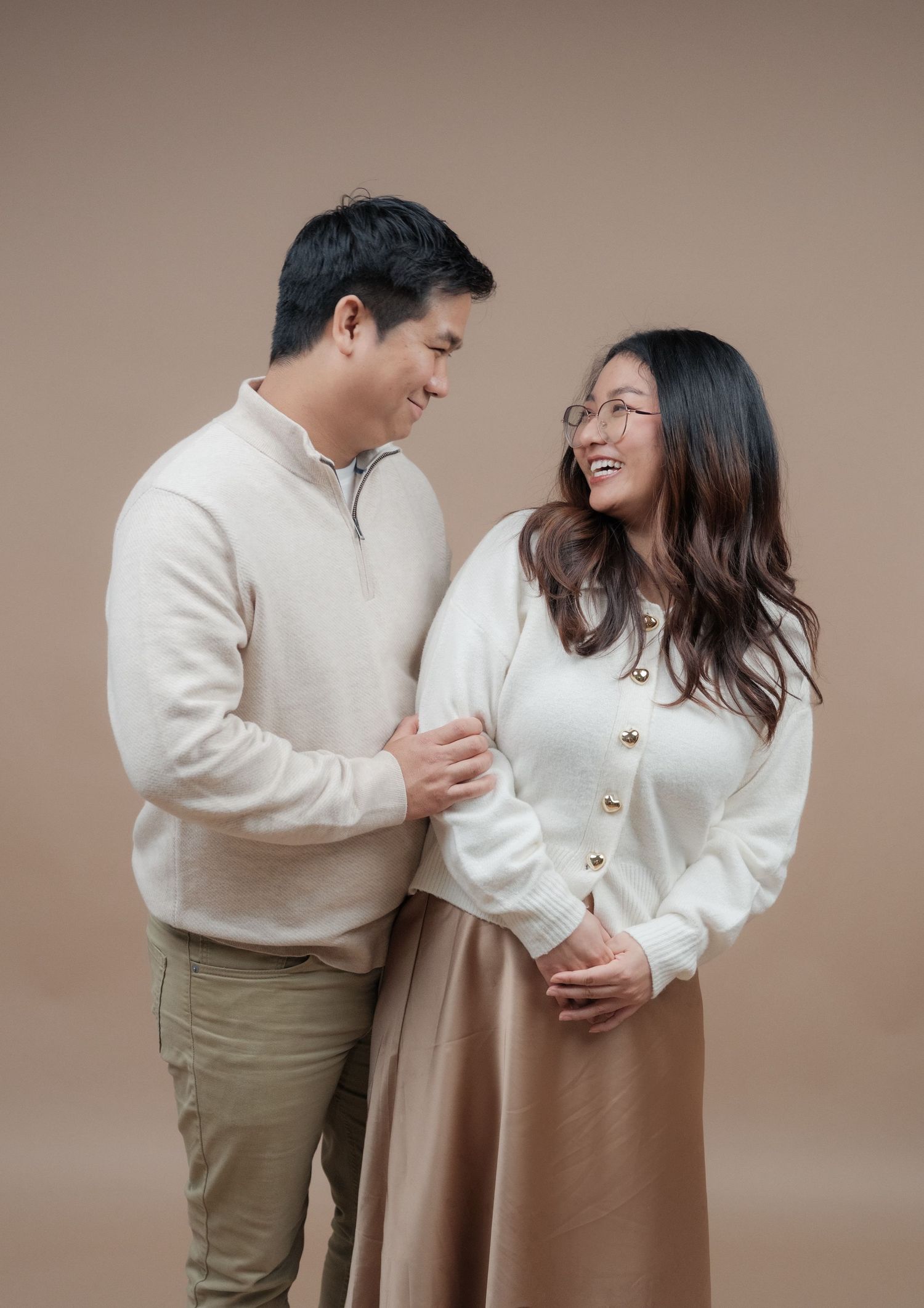 Couple in coordinating cream outfits share intimate laugh during photo session.