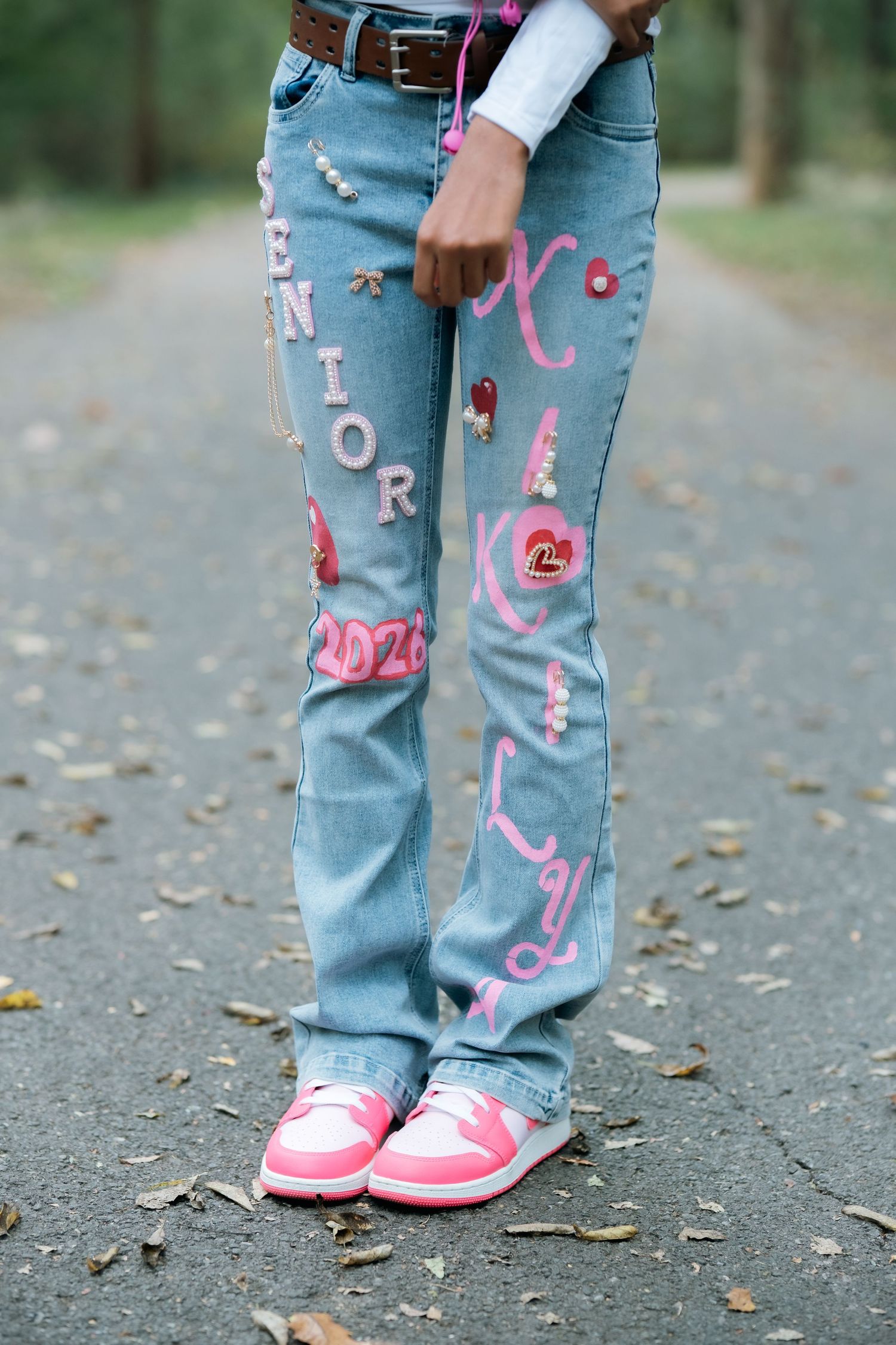 Close-up of decorated light blue jeans with pink painted designs and details.