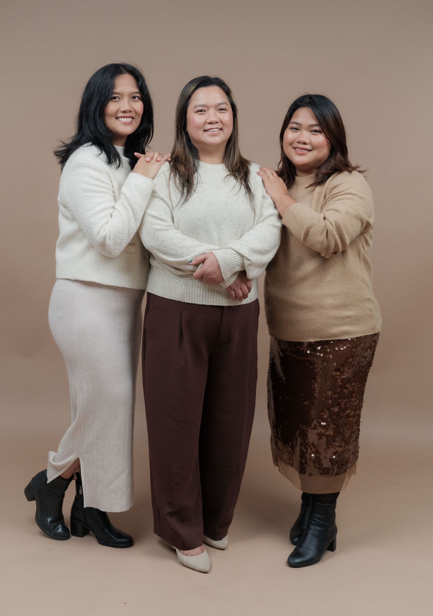 Three people in coordinating cream and brown outfits pose casually against a neutral backdrop.