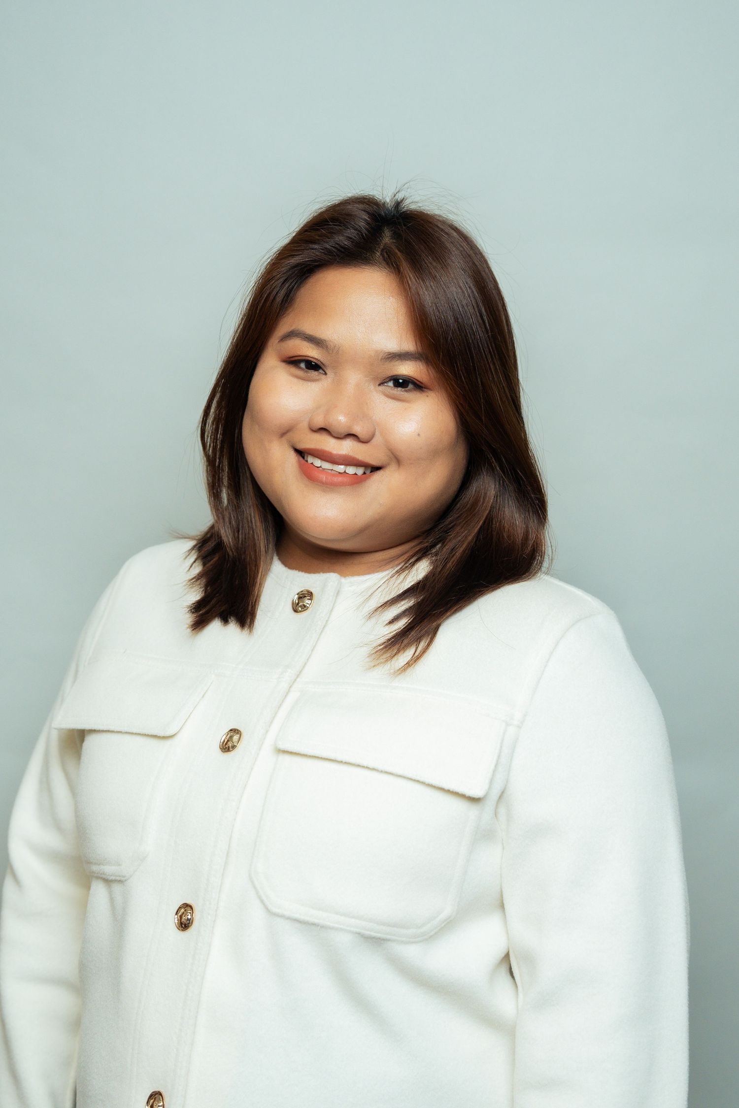 Professional portrait of person in white button-up jacket against light background.