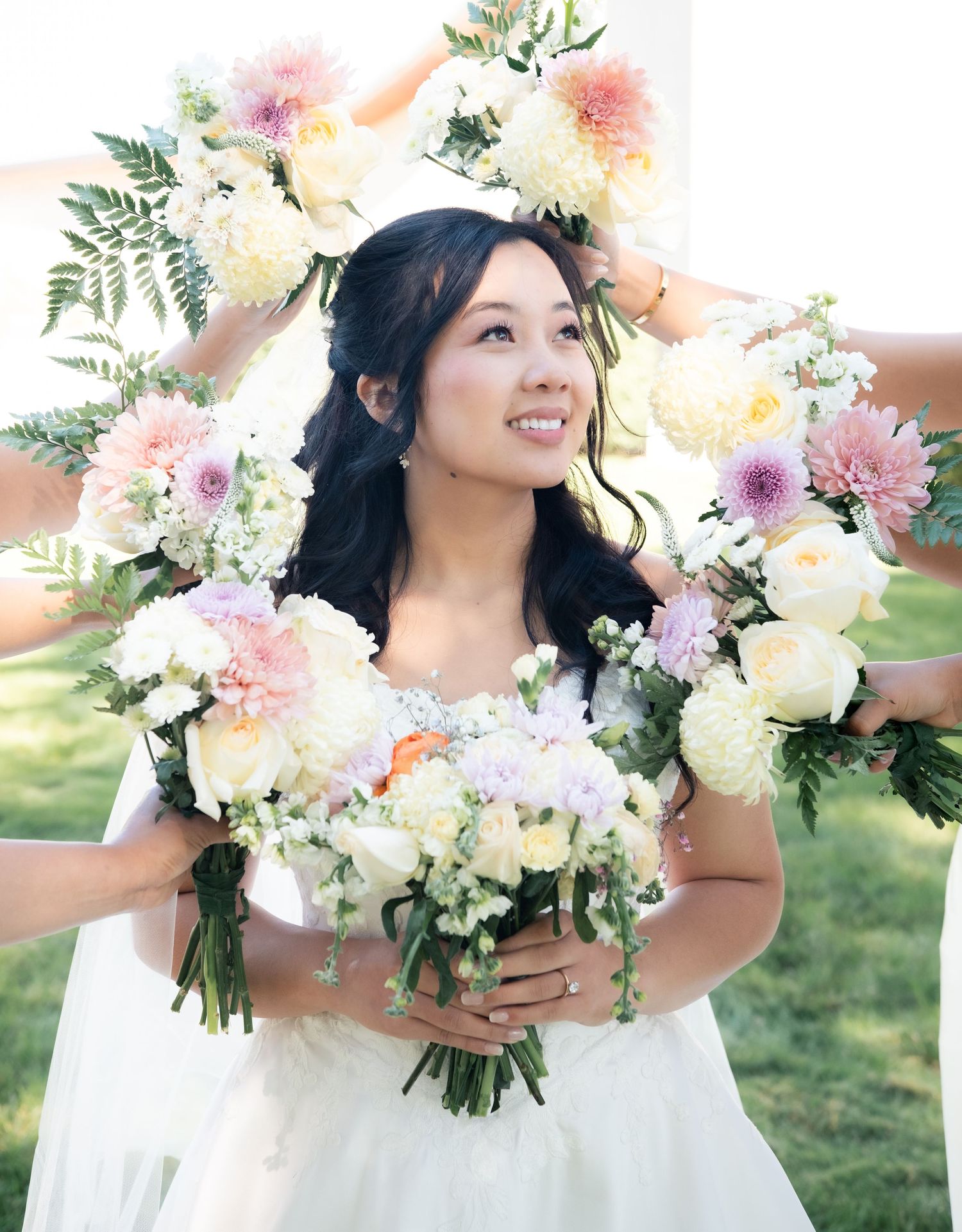 Bride wearing floral crown holds pastel bouquet with pink and white flowers surrounded by decorative arrangements.