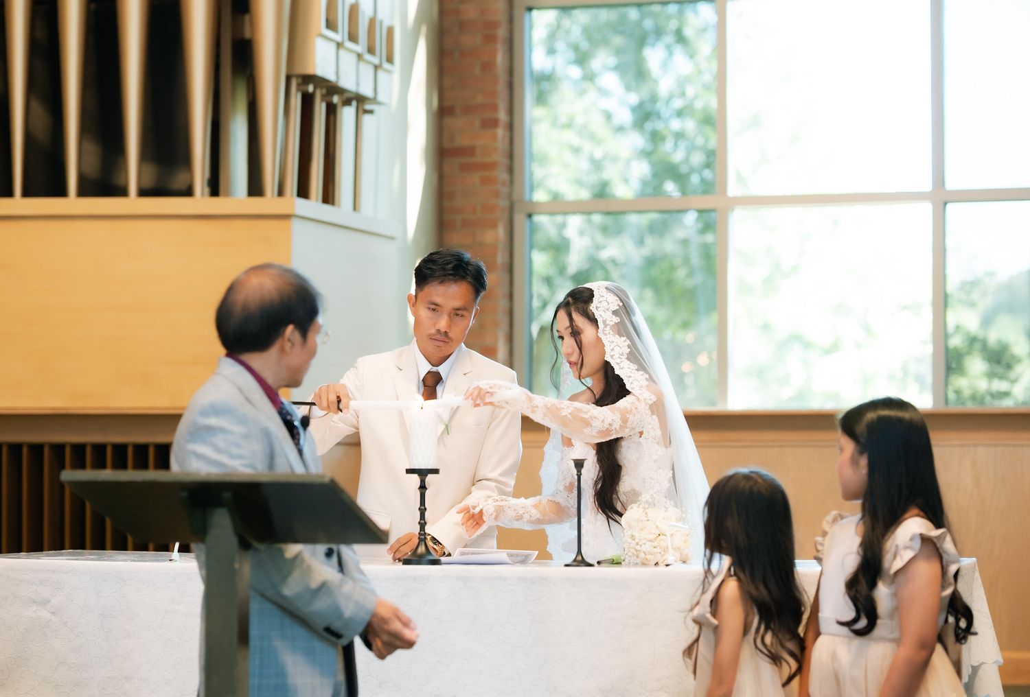 Bride and groom perform unity candle ceremony at church altar with officiant and guests during elegant wedding.