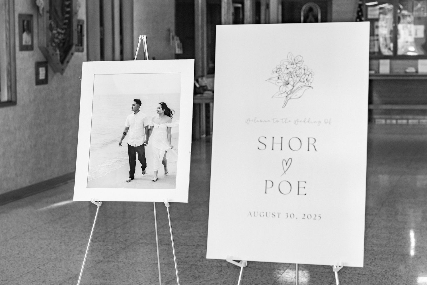 Black and white wedding signage display with photo stands in venue hallway.