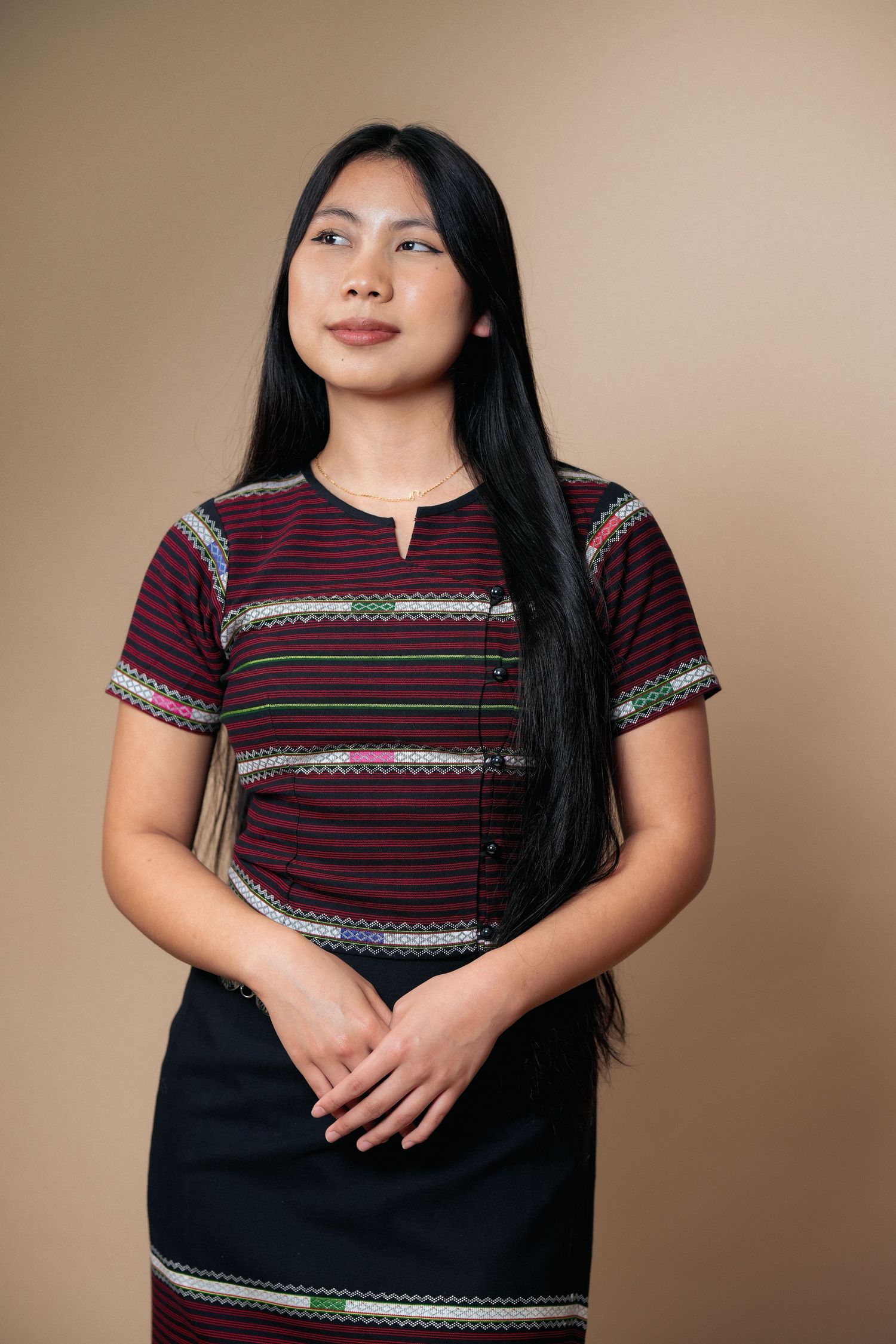 Studio portrait showcasing burgundy and black traditional outfit with decorative details.