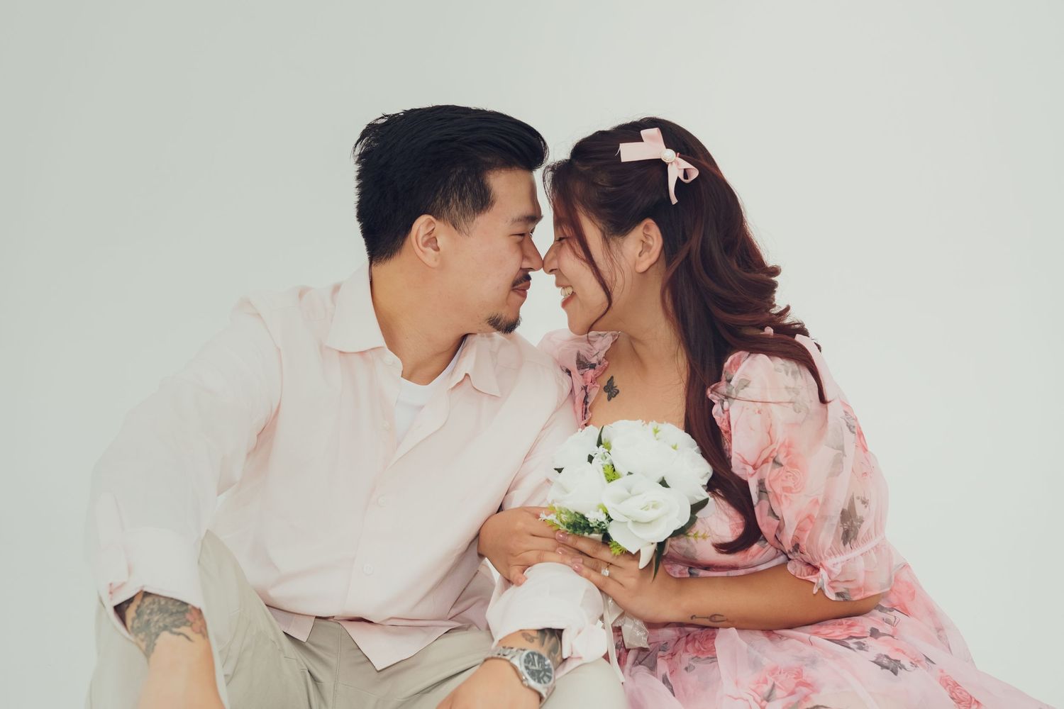 Couple shares intimate moment in pink and white outfits against light background.
