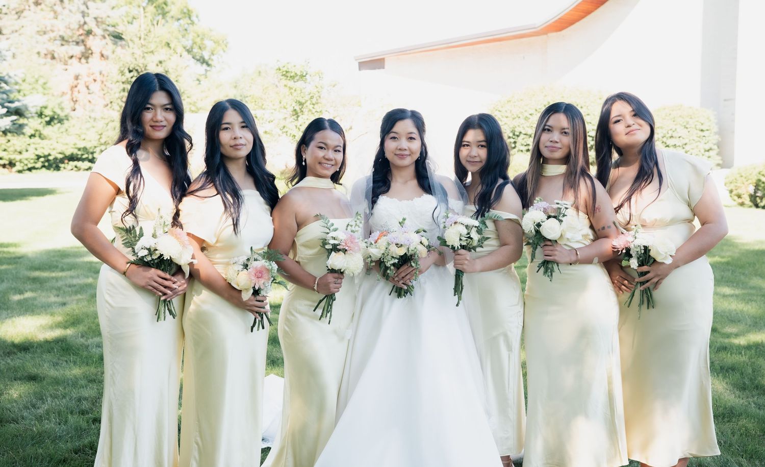 Bridal party in cream colored dresses standing together outdoors with bouquets.