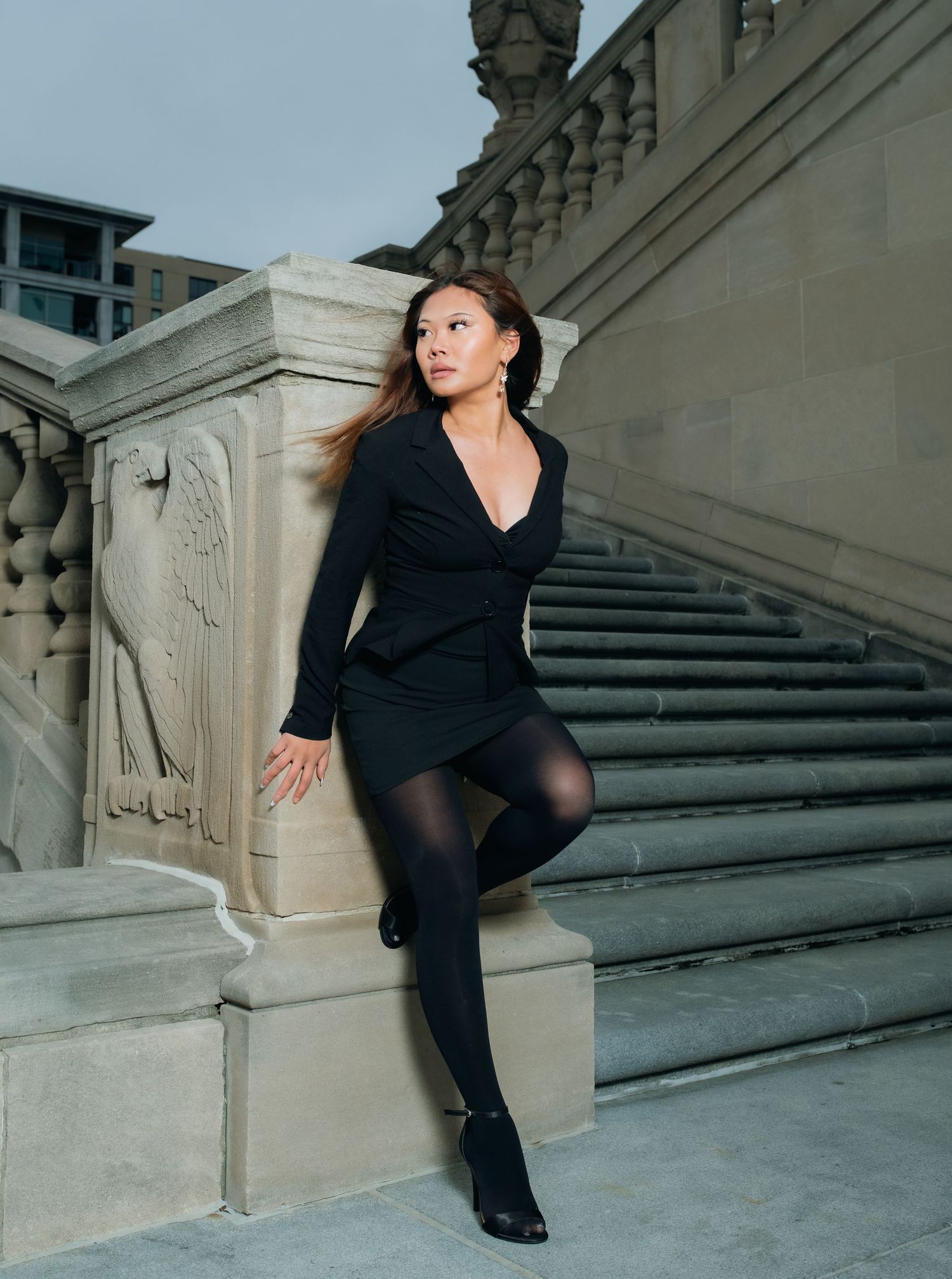 A dancer in black attire performs an elegant pose on a grand stone staircase.