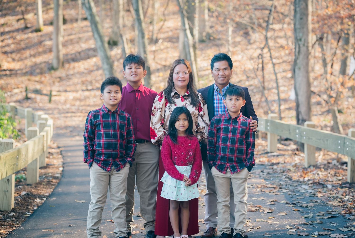 A family group poses together on a wooded path covered in fallen autumn leaves.