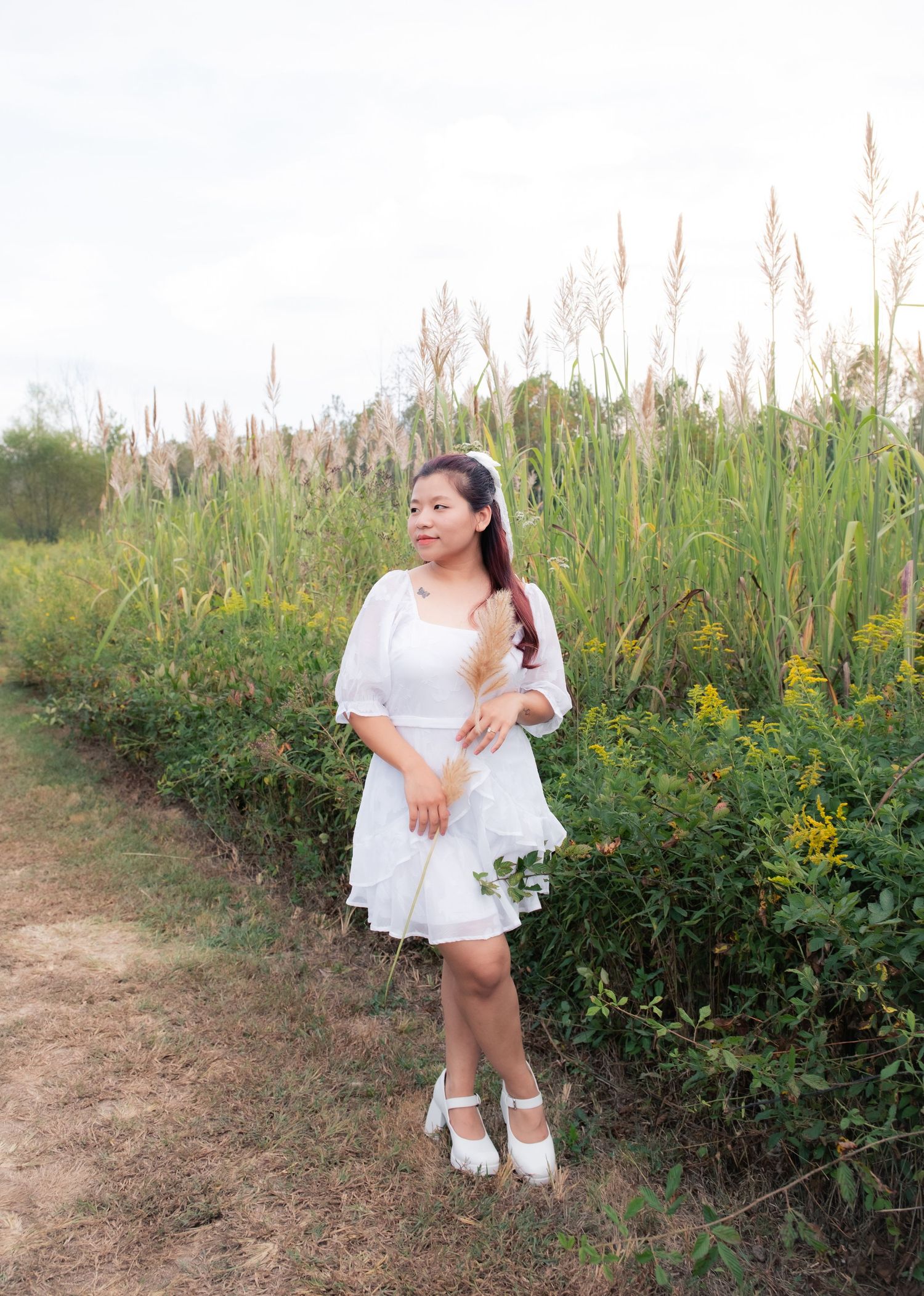 A person in a white dress poses gracefully in a field of tall grass and wildflowers.