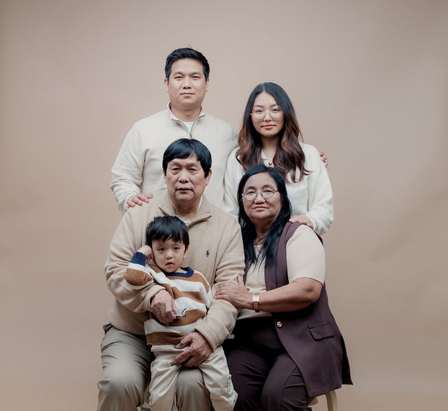 Multi-generational family in neutral tones poses together for formal portrait.