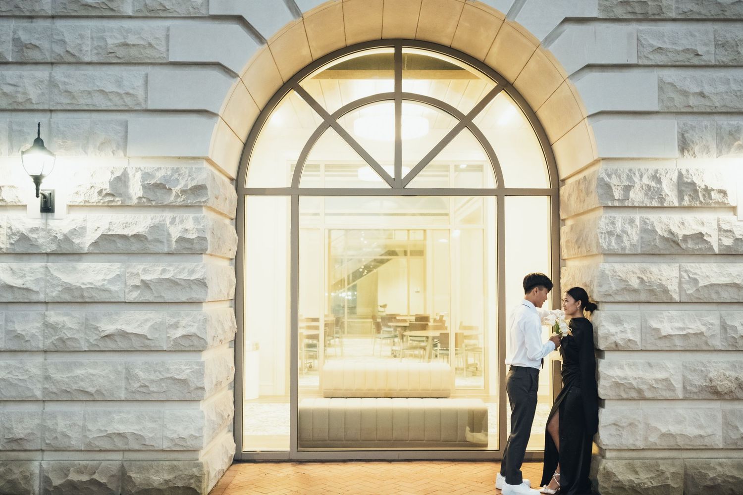 People walking through a stone corridor with dramatic arched windows and natural light.