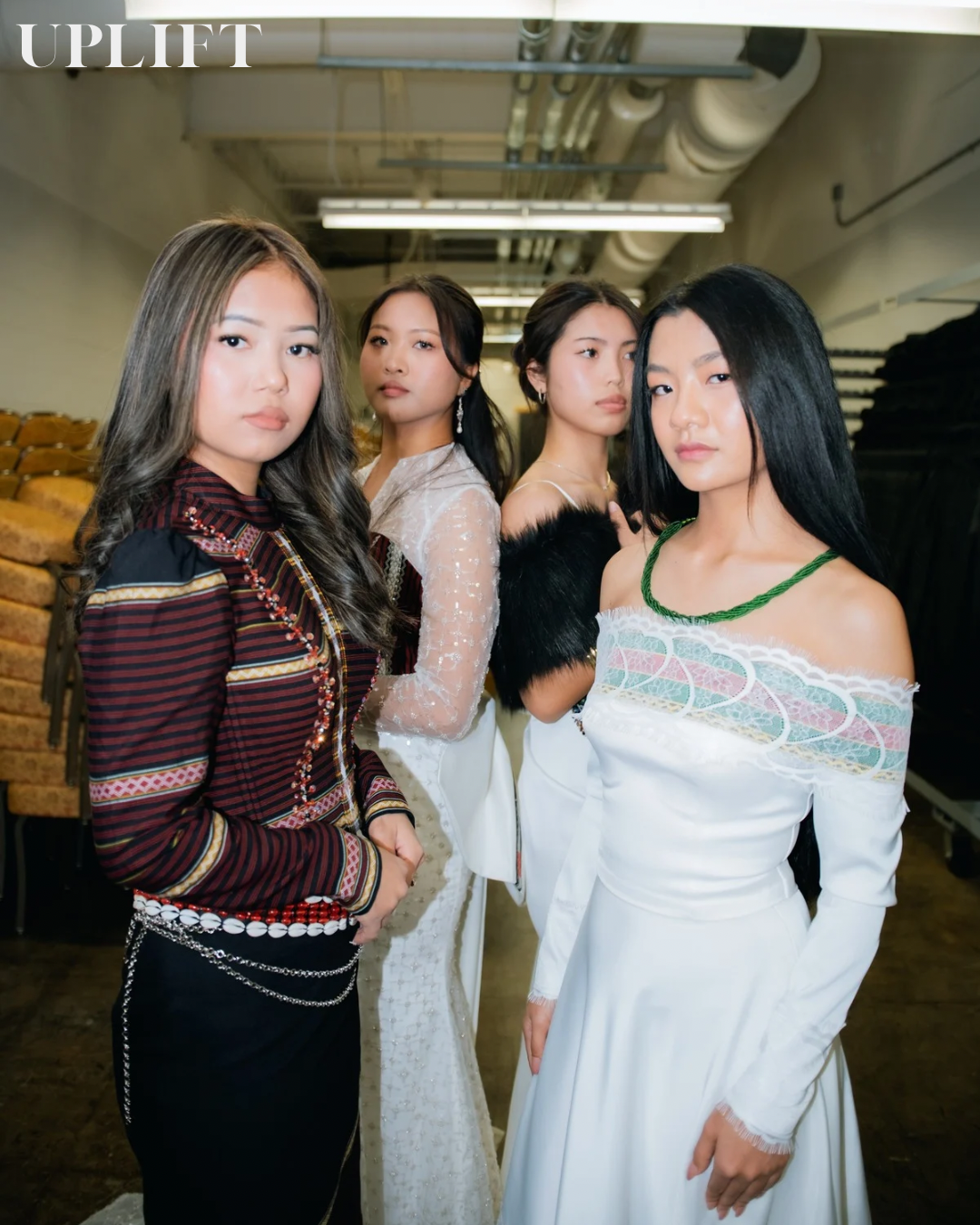 Models in elegant white dresses and dark knit tops pose together in a studio setting.