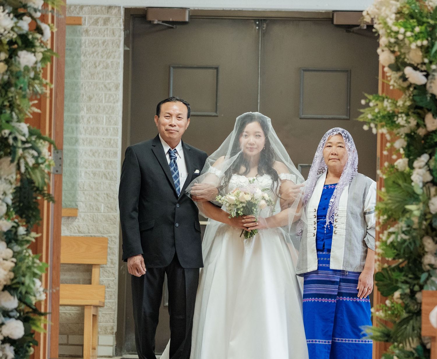 Wedding ceremony with floral arch and couple with family member during processional.