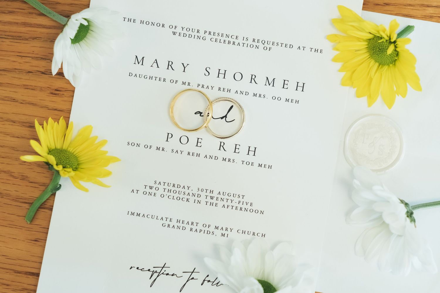 Wedding invitation with yellow daisies and white flowers on wooden surface.