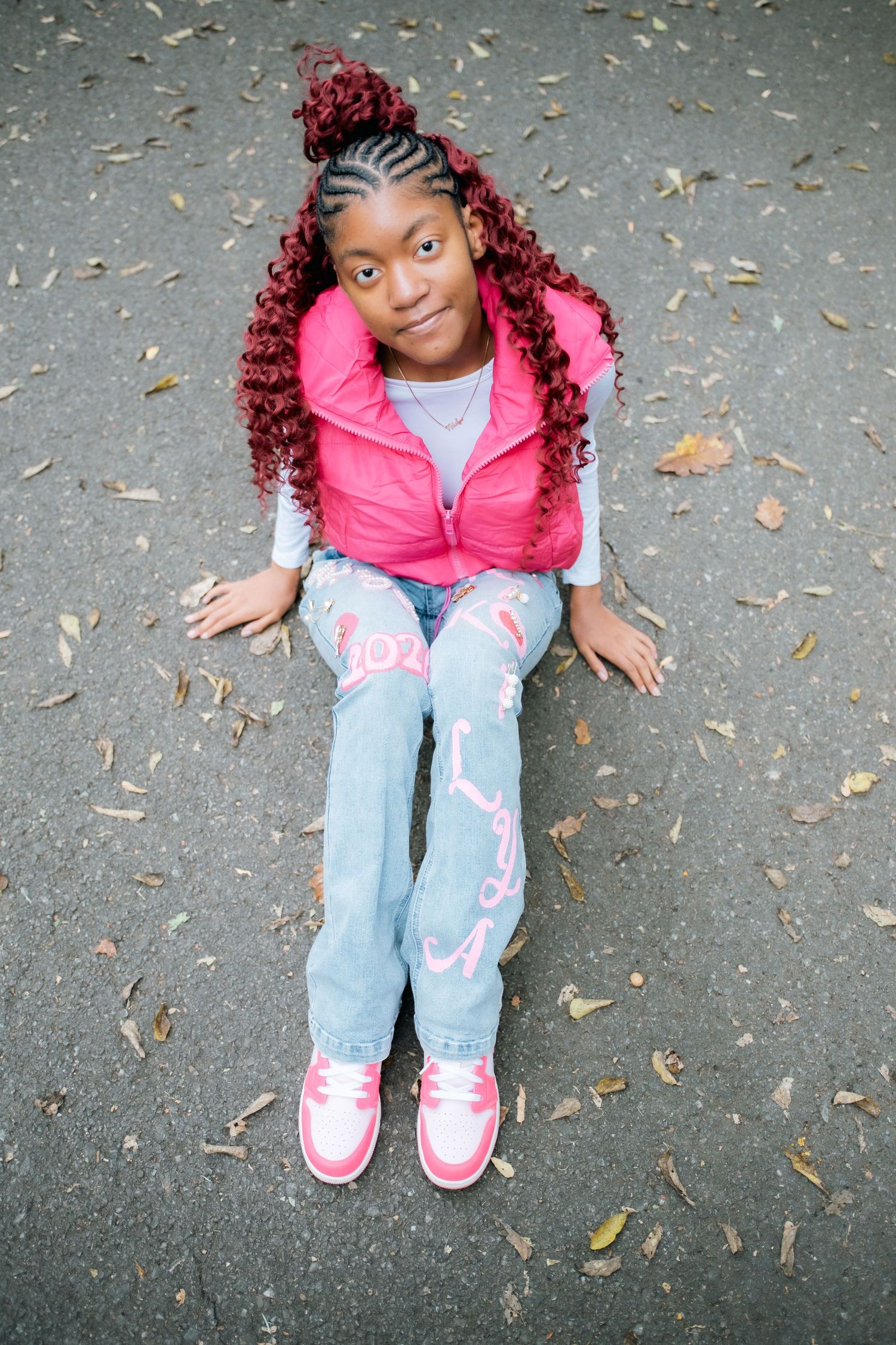 Overhead view of someone sitting on pavement wearing pink vest and decorated jeans.