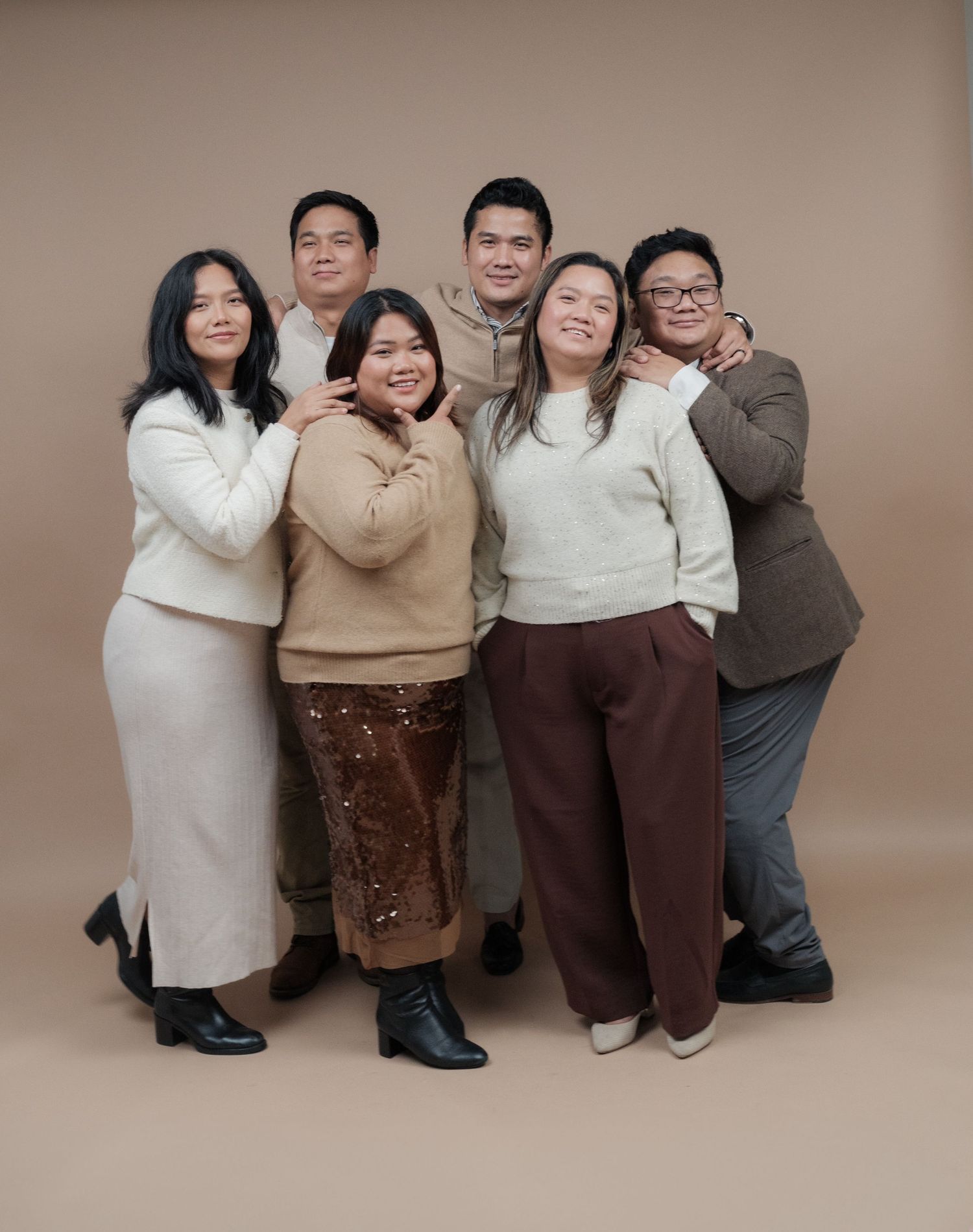Group of seven people in coordinated neutral outfits pose together for a casual studio portrait.