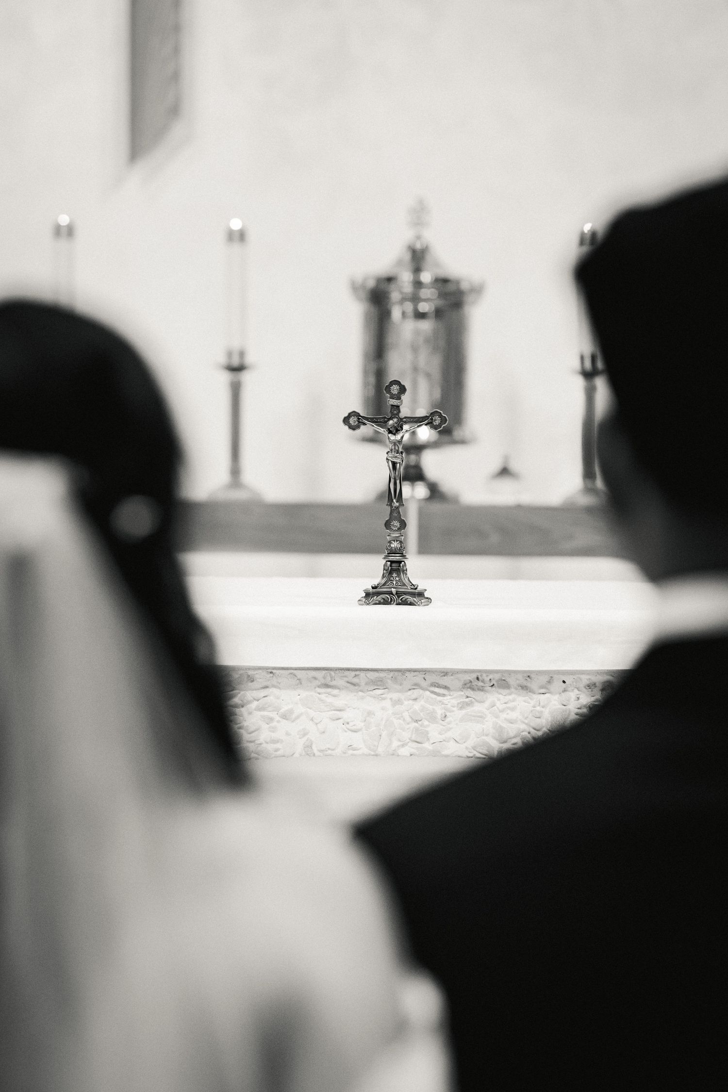 A crucifix stands prominently on an altar with silhouettes of attendees in the foreground during a church ceremony.