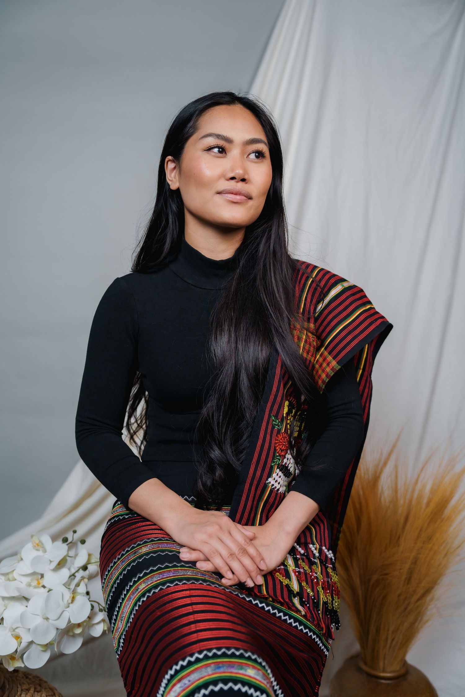 Portrait session featuring traditional textile wrap and black top against minimalist studio backdrop.