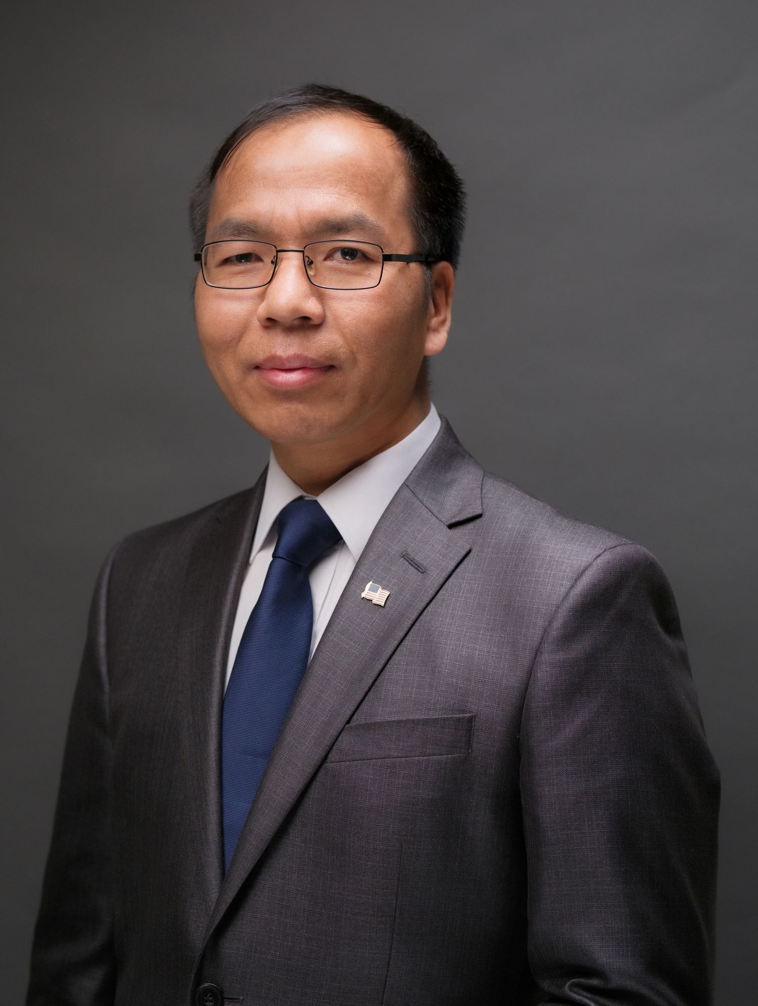Professional Asian man in gray suit and blue tie poses for formal business portrait photo.
