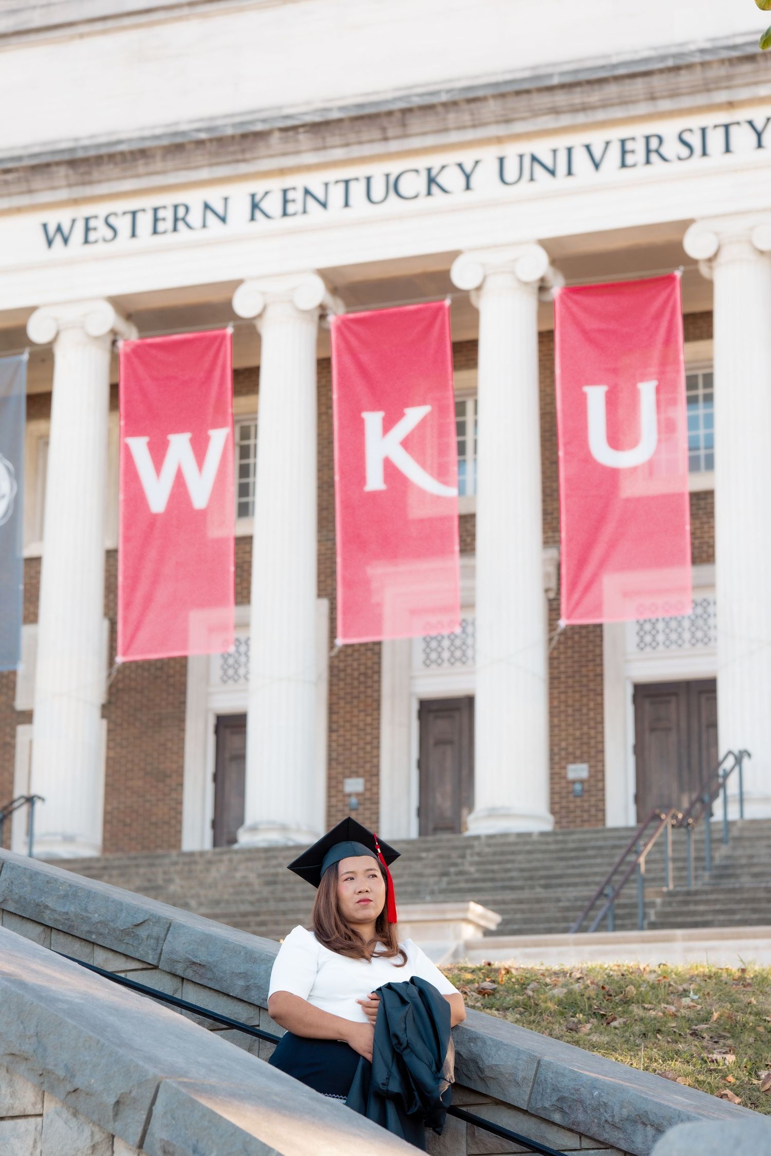 Graduate reclining on campus steps with Western Kentucky University banners.